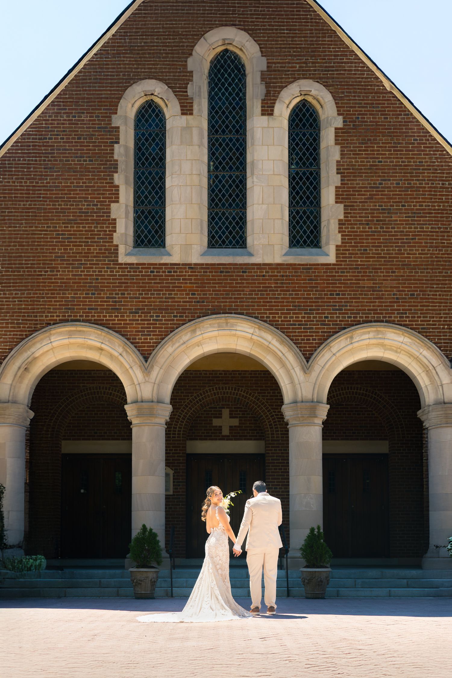 A couple stands in silhouette against arched brick architecture with gothic windows and stone columns.
