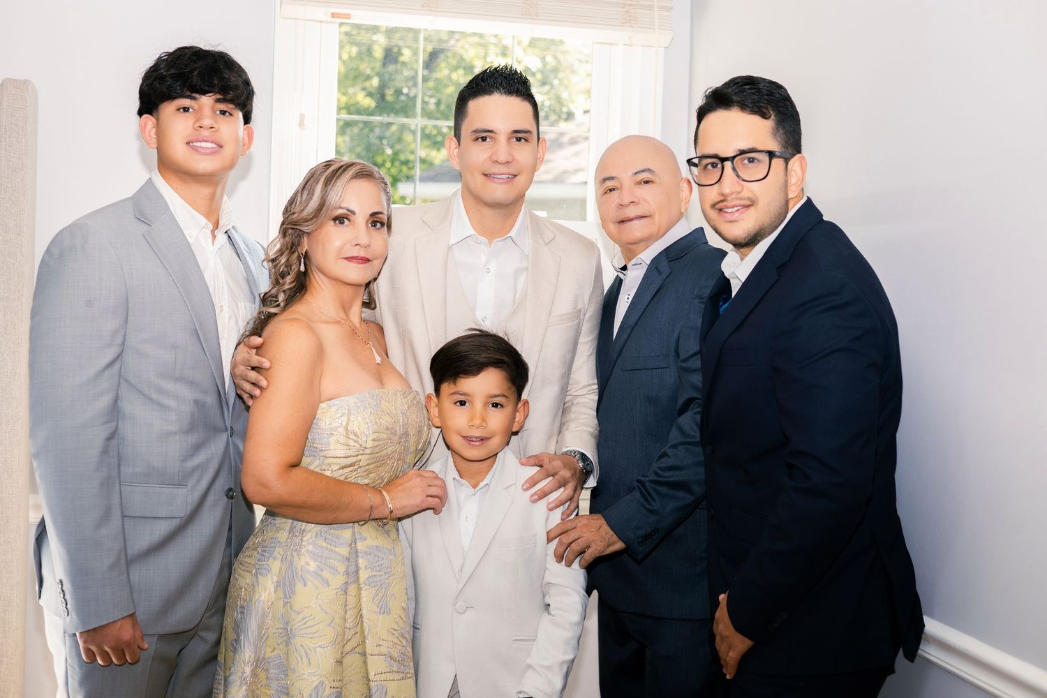 Wedding party members in formal attire pose together for group photos in light-filled indoor setting.