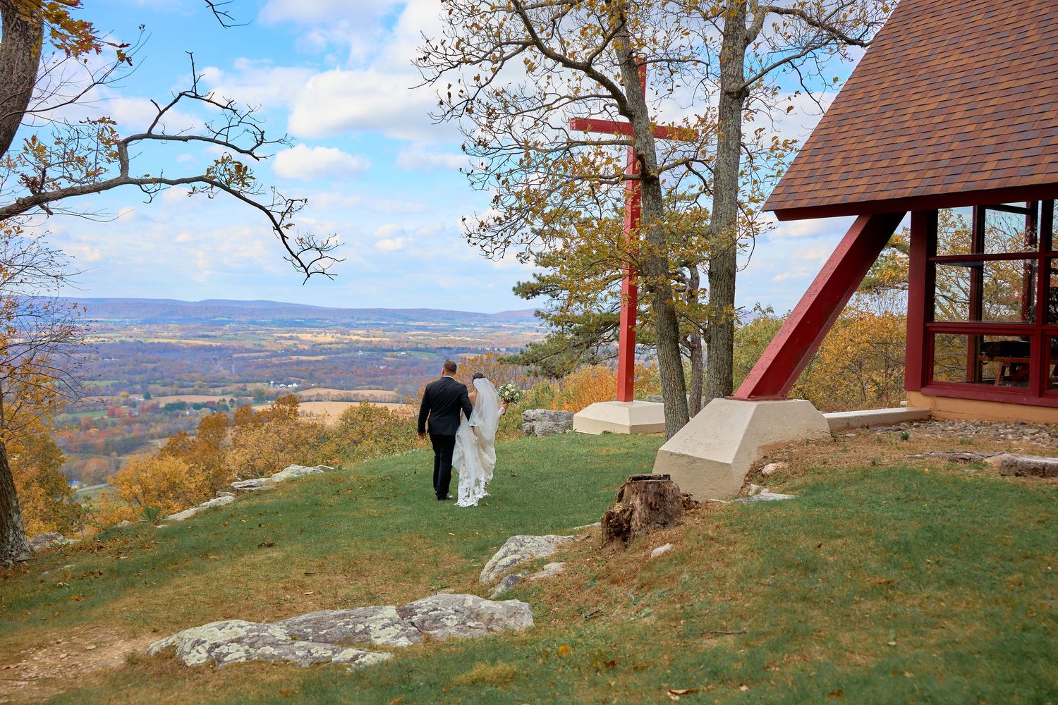 Scenic autumn landscape with red cabin overlooking rolling hills and distant mountains on a sunny day.