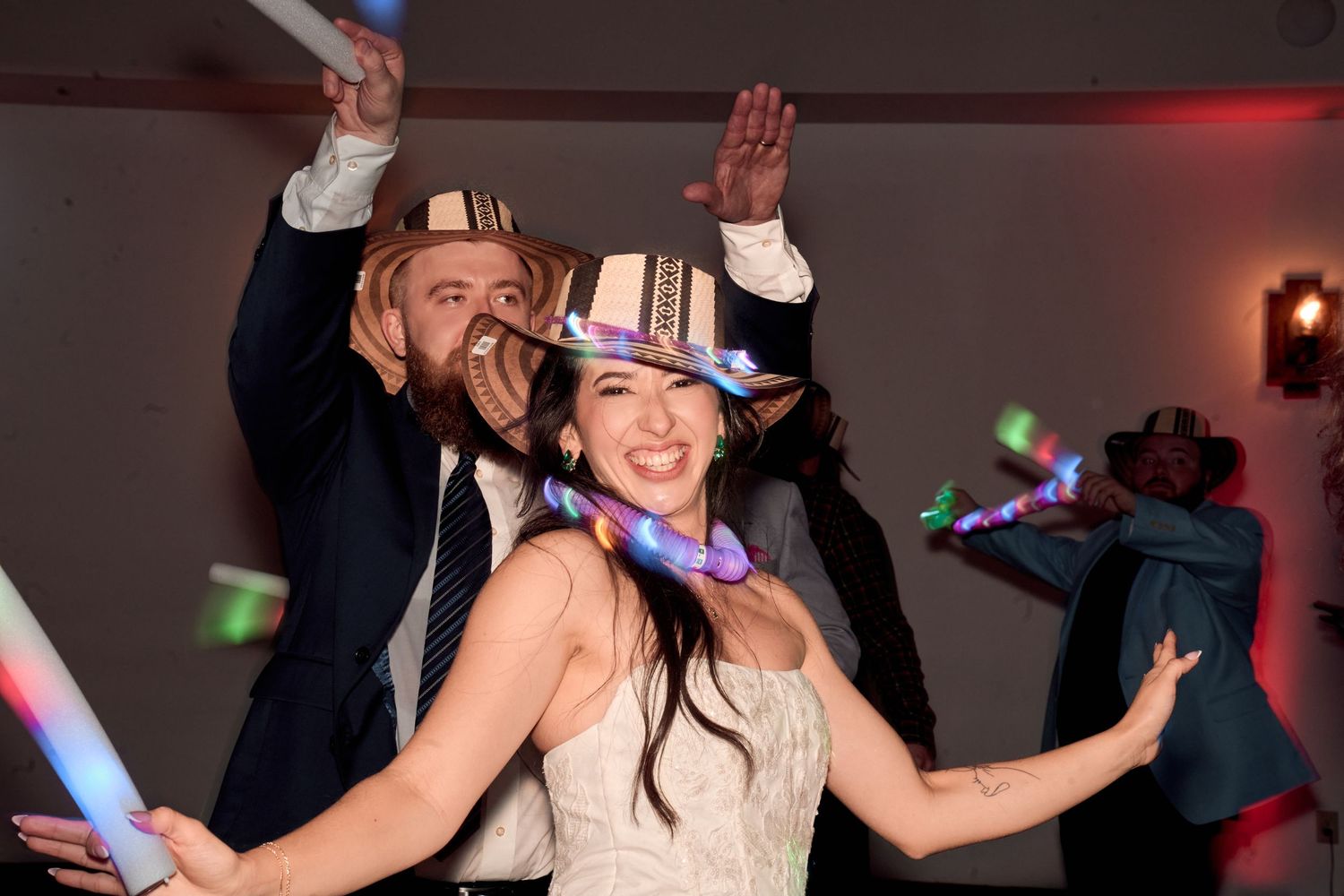 Wedding guests celebrate on the dance floor with glow sticks and party props.