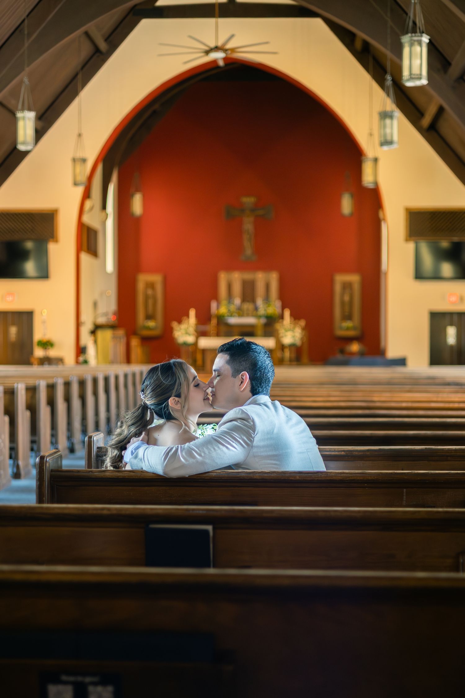 A couple shares an intimate moment in a church pew with stained glass windows and wooden architecture visible.