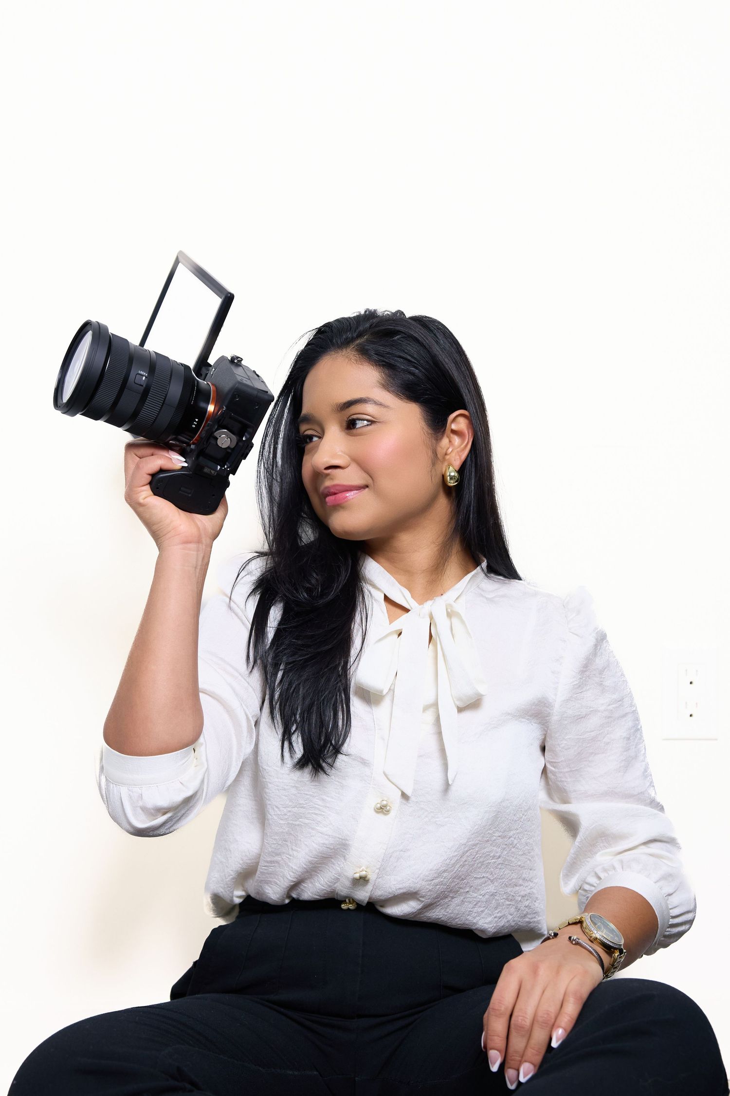 A person in a white hoodie poses with a camera against a white backdrop.