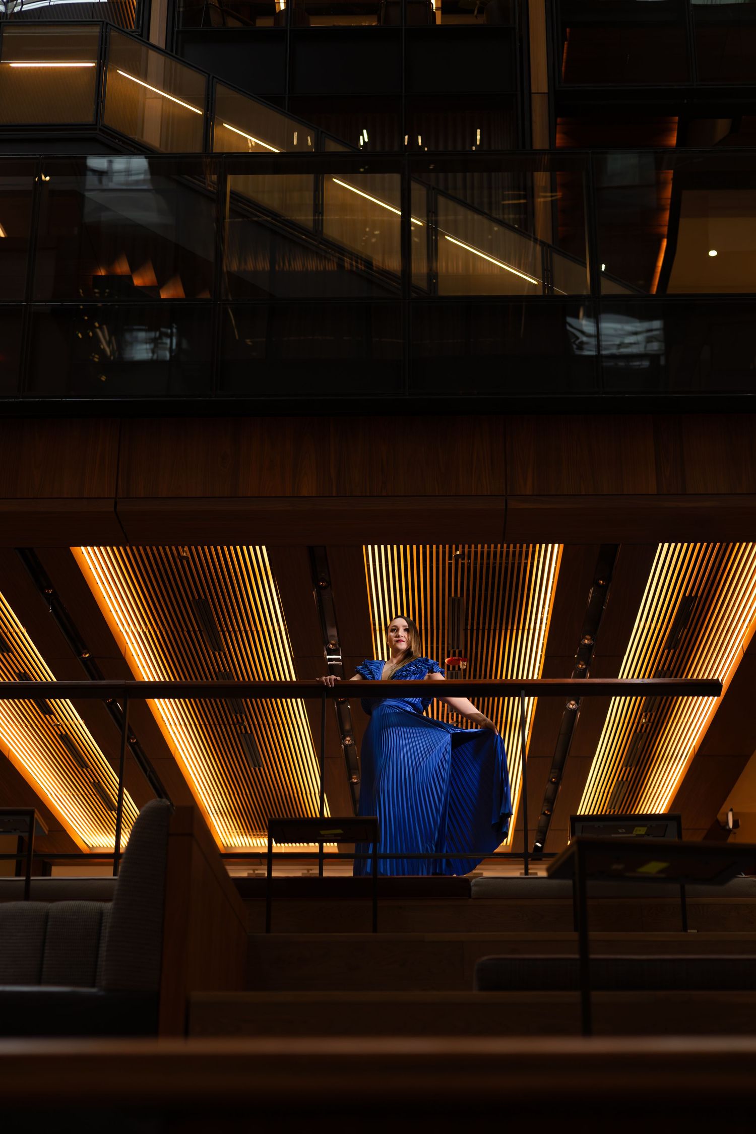 Silhouette of person in blue dress against geometric interior with warm lighting.