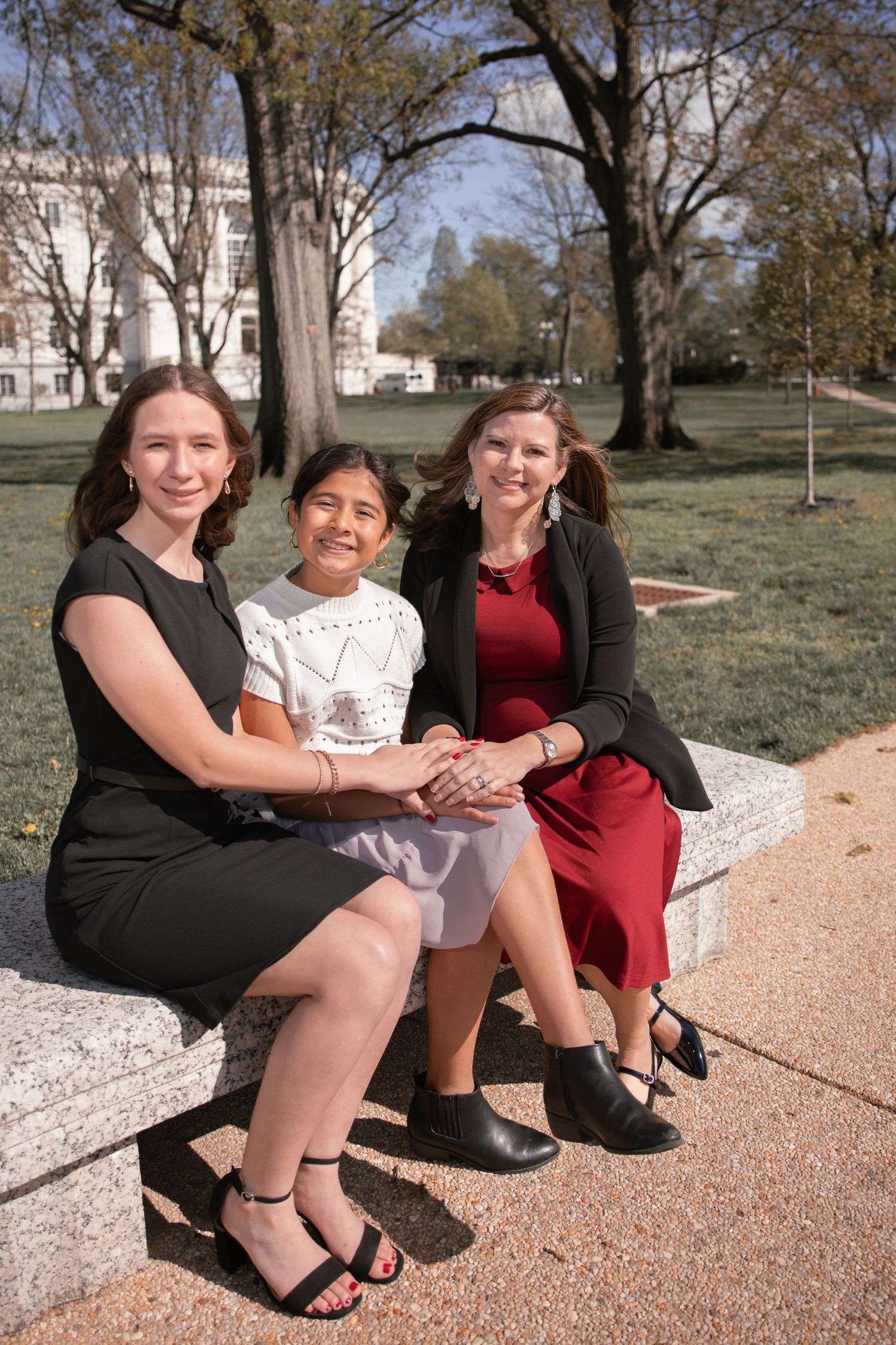 Three people sitting together on stone steps in an outdoor setting with trees and a building in the background.