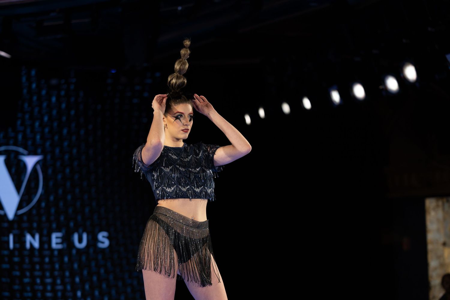 Dancer performs on stage in fringe costume with dramatic lighting.