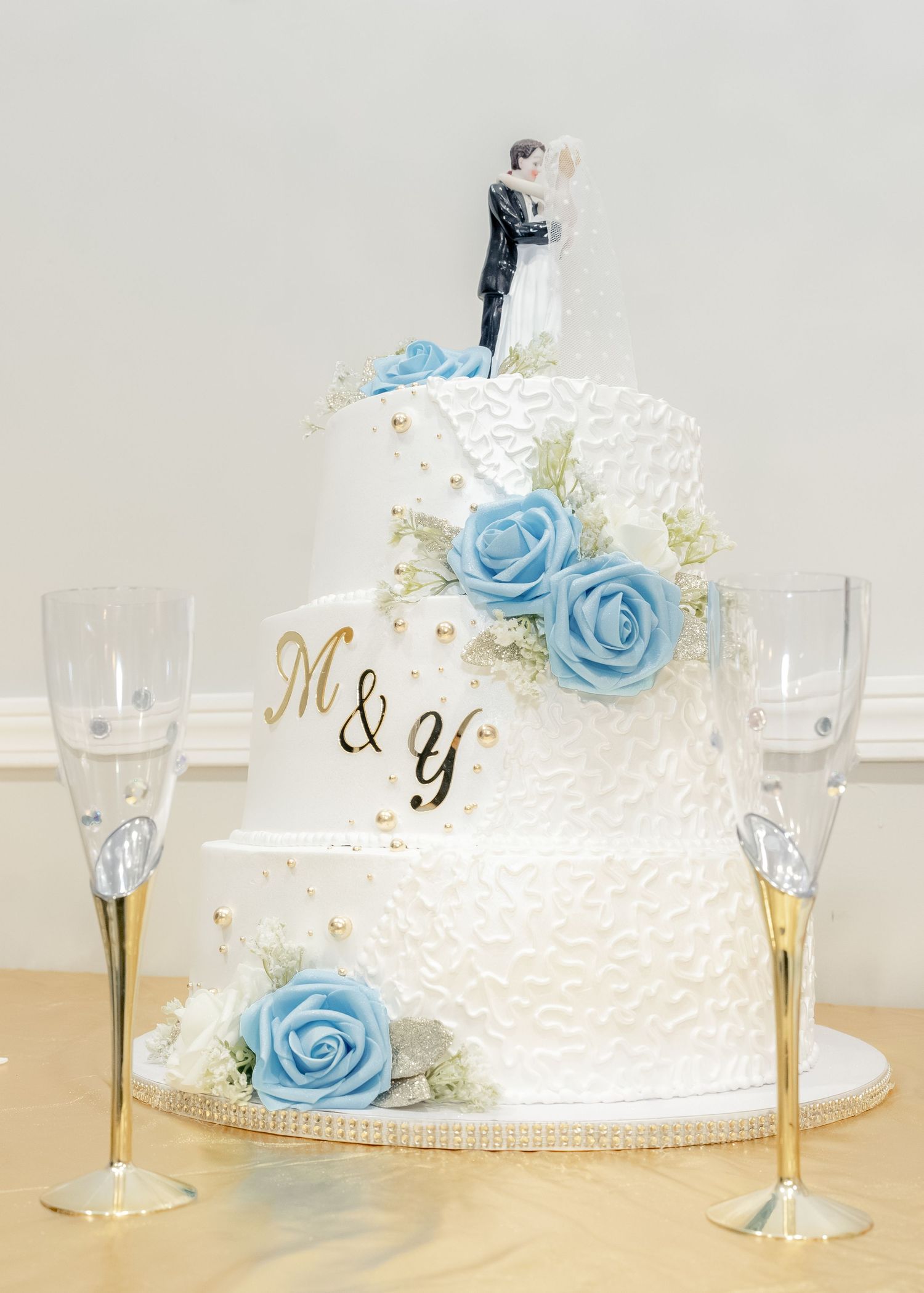 Elegant white wedding cake decorated with light blue roses and bride and groom topper.
