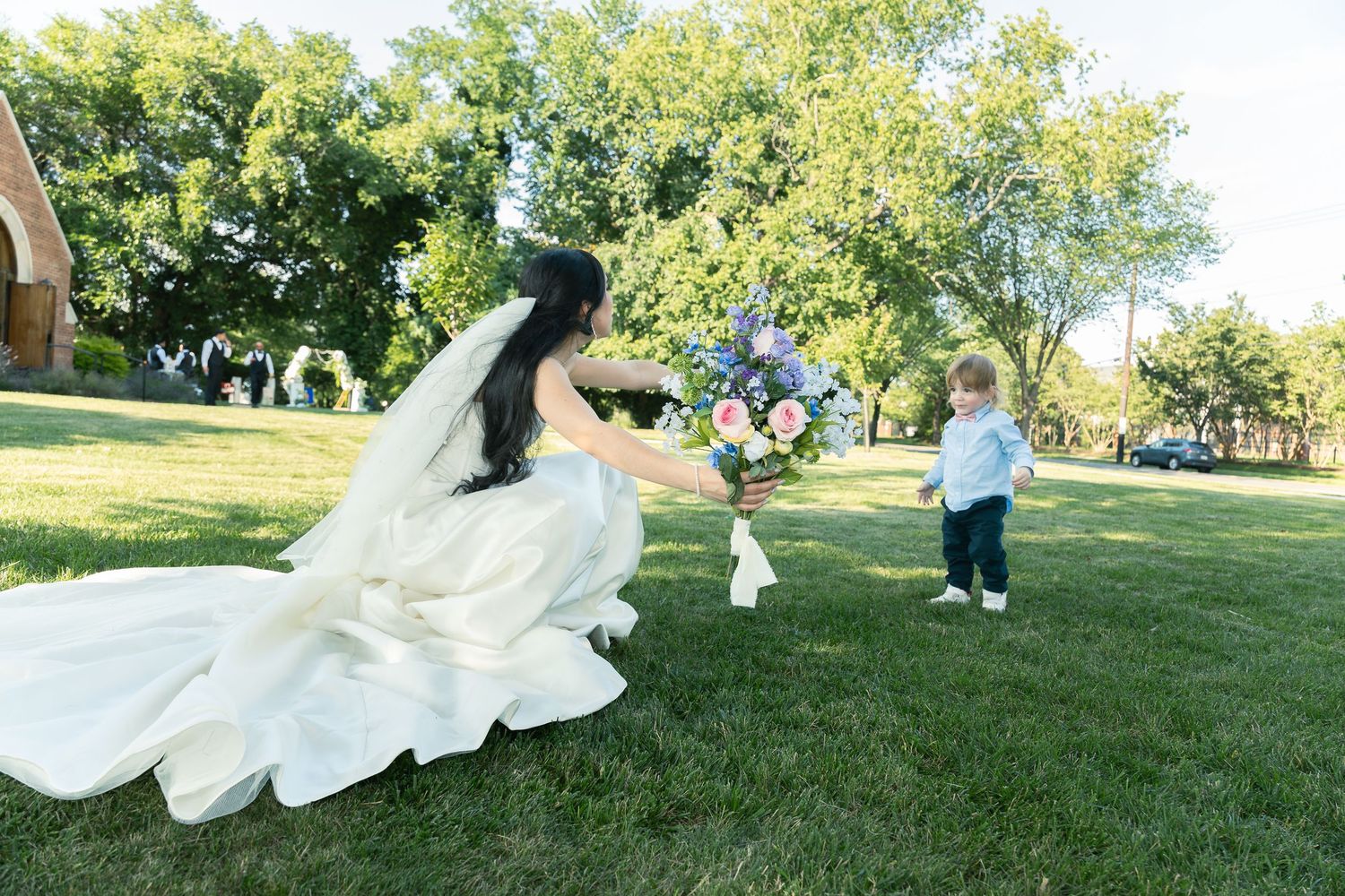 Two people in wedding formal wear run playfully through a sunny green park while being photographed outdoors.