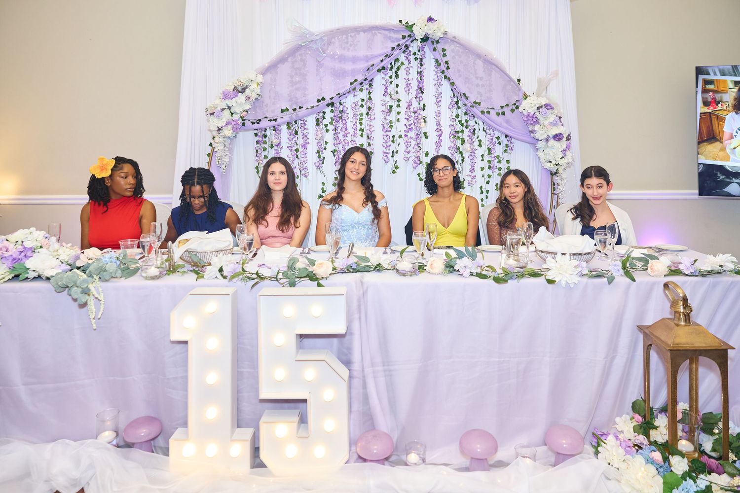 Wedding reception banquet hall decorated in lavender and white with floral arrangements and string lights.