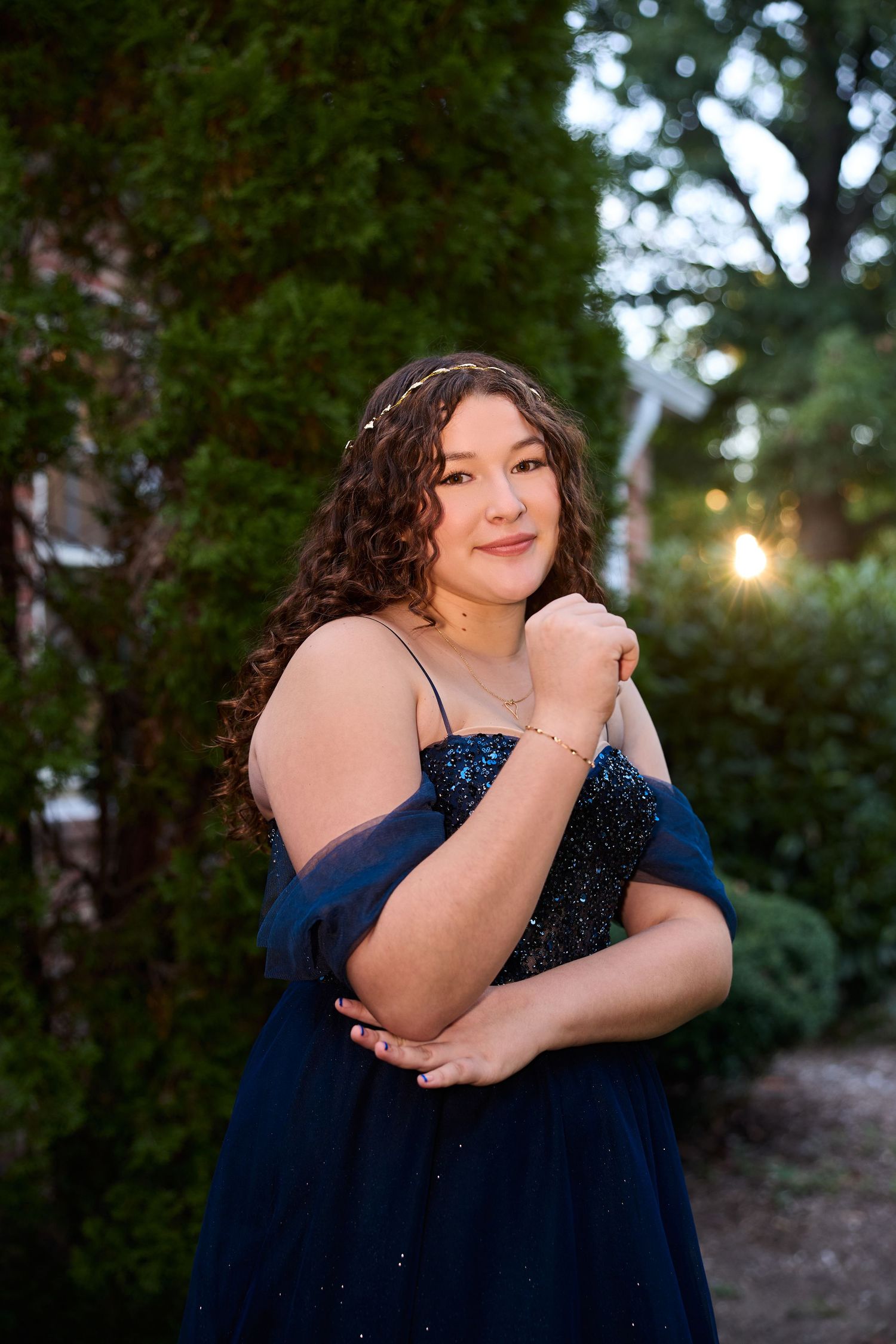 A person in a sparkly navy blue dress poses outdoors in a natural garden setting at dusk.