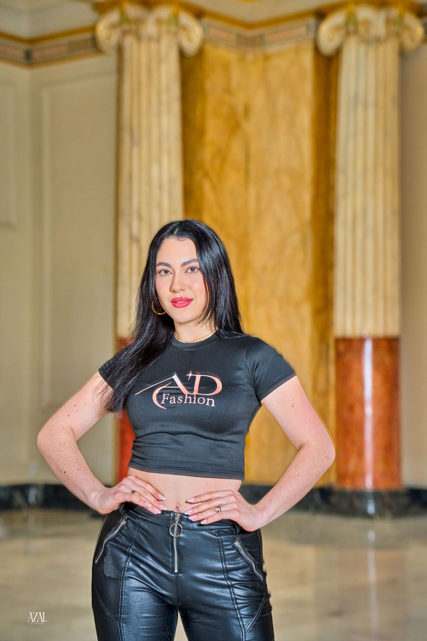 Woman posing in AD Fashion black crop top and leather pants in elegant marble columned hall.