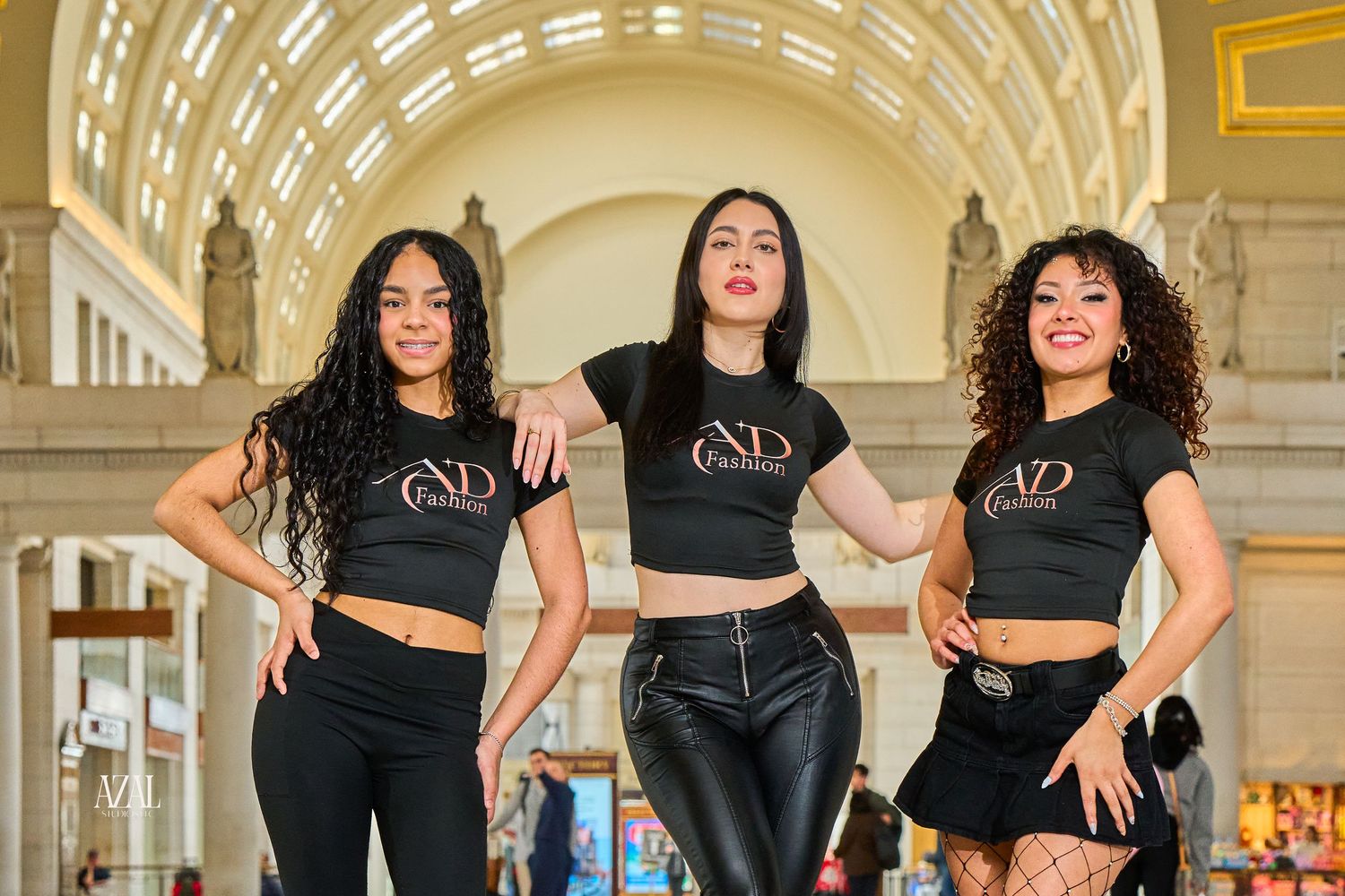 Three women in matching black crop tops and pants pose confidently inside an elegant building with arched ceilings.