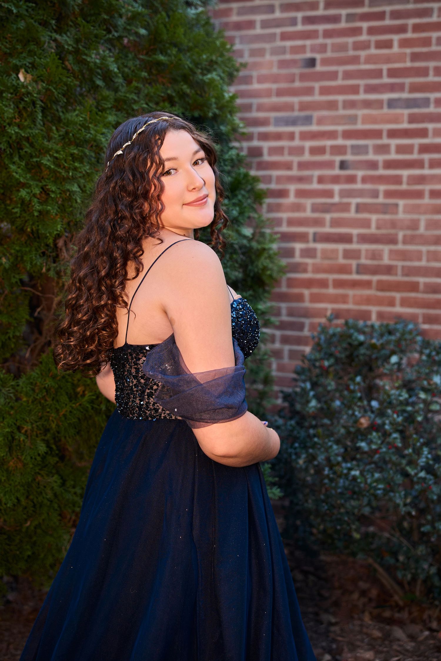 A series of photos showing someone in a sparkly navy blue formal dress posing against a brick wall with greenery.