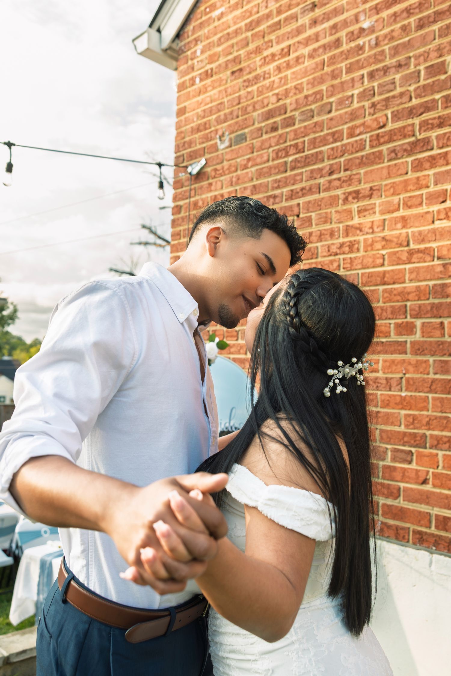 A romantic couple in white and blue outfits share intimate moments against a brick wall background.