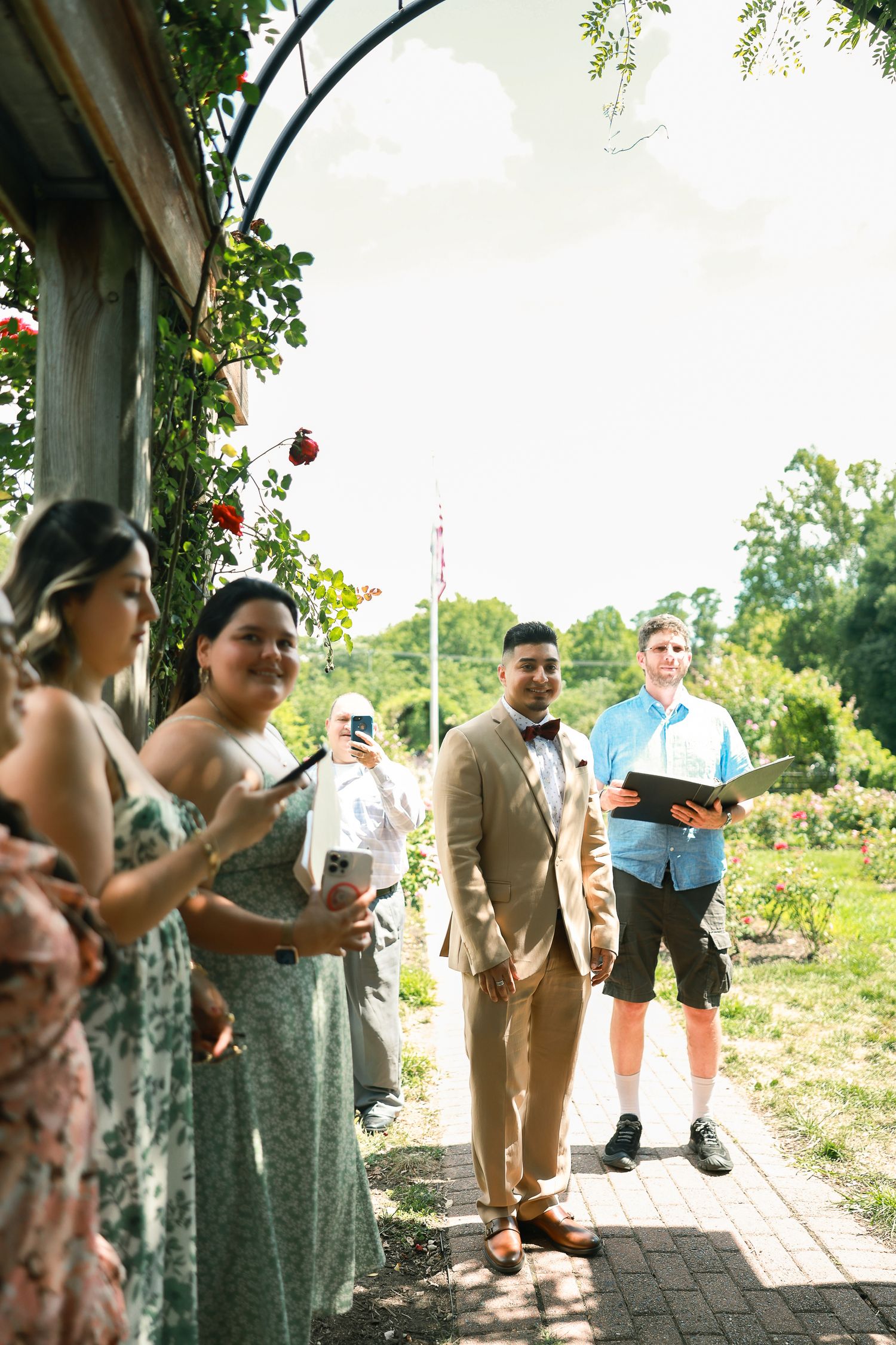 Wedding ceremony under an arch with guests gathered in summer garden setting.