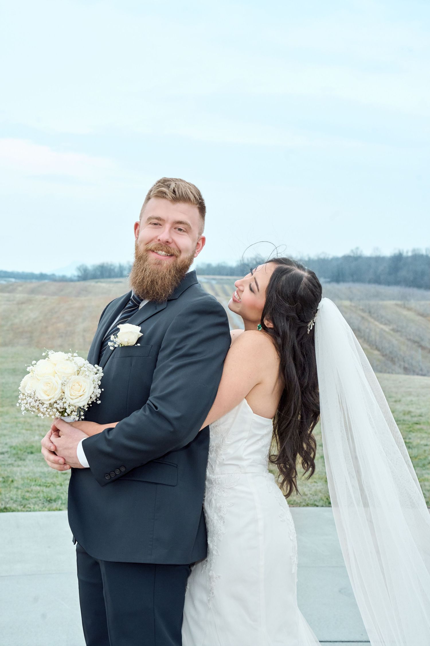A happy couple shares joyful moments during their outdoor wedding photoshoot in a scenic hillside setting.