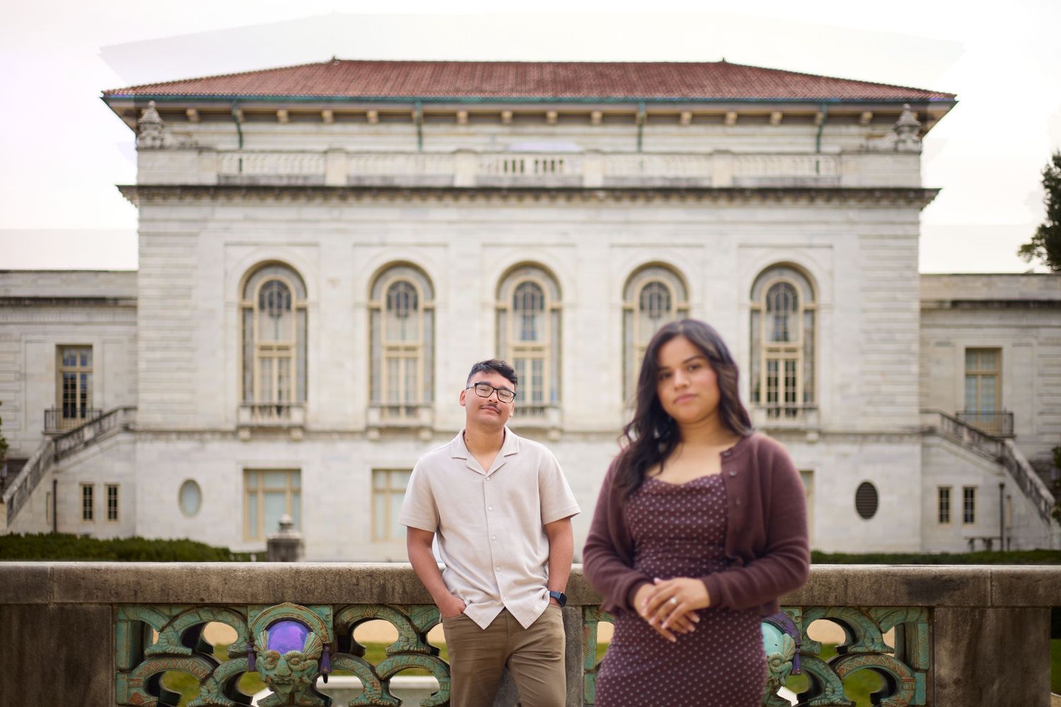 A couple poses for engagement photos in front of a grand white stone building with classical architecture.