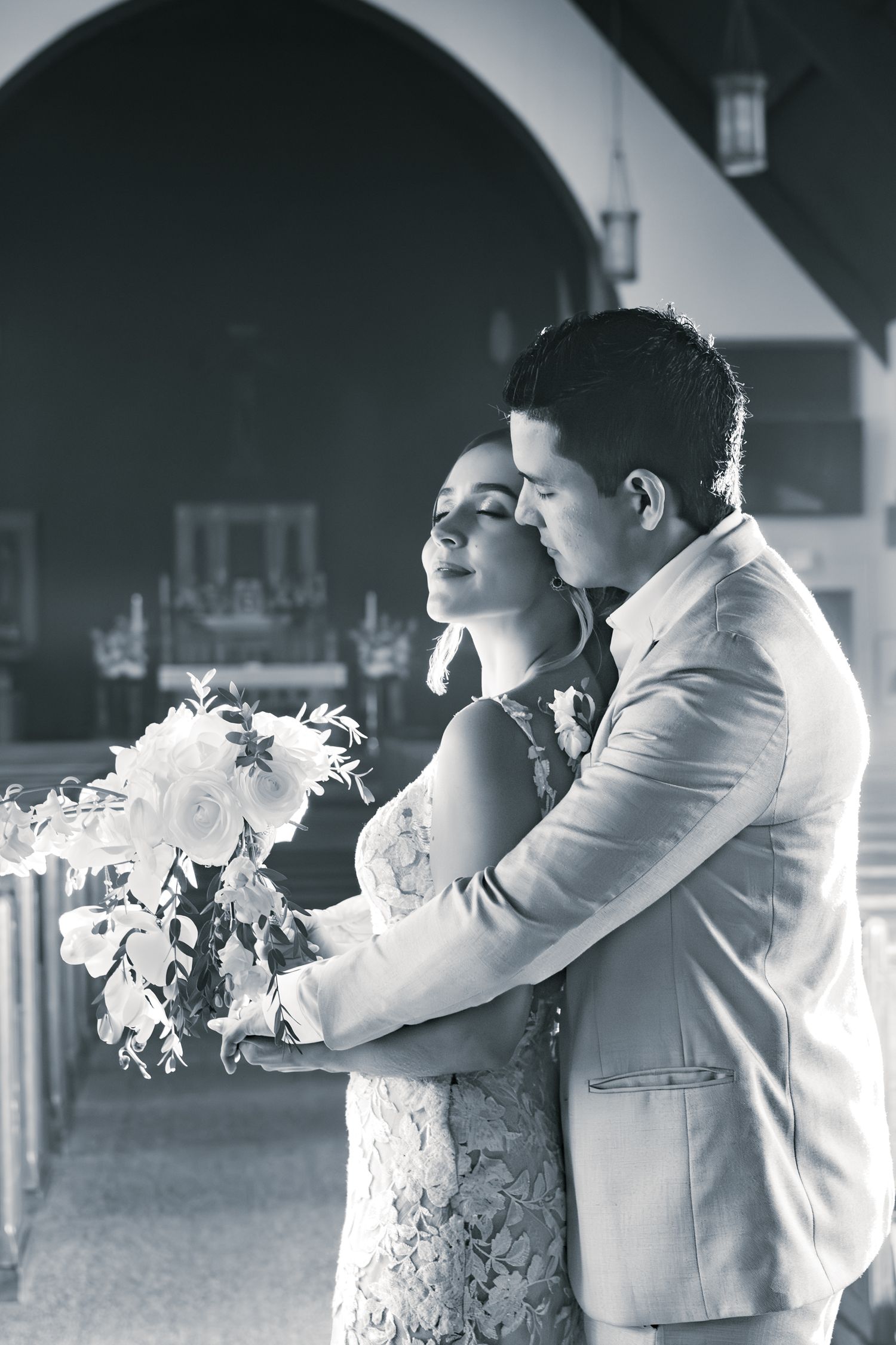 A romantic black and white wedding photo shows a couple embracing, with the bride holding a bouquet of white flowers.