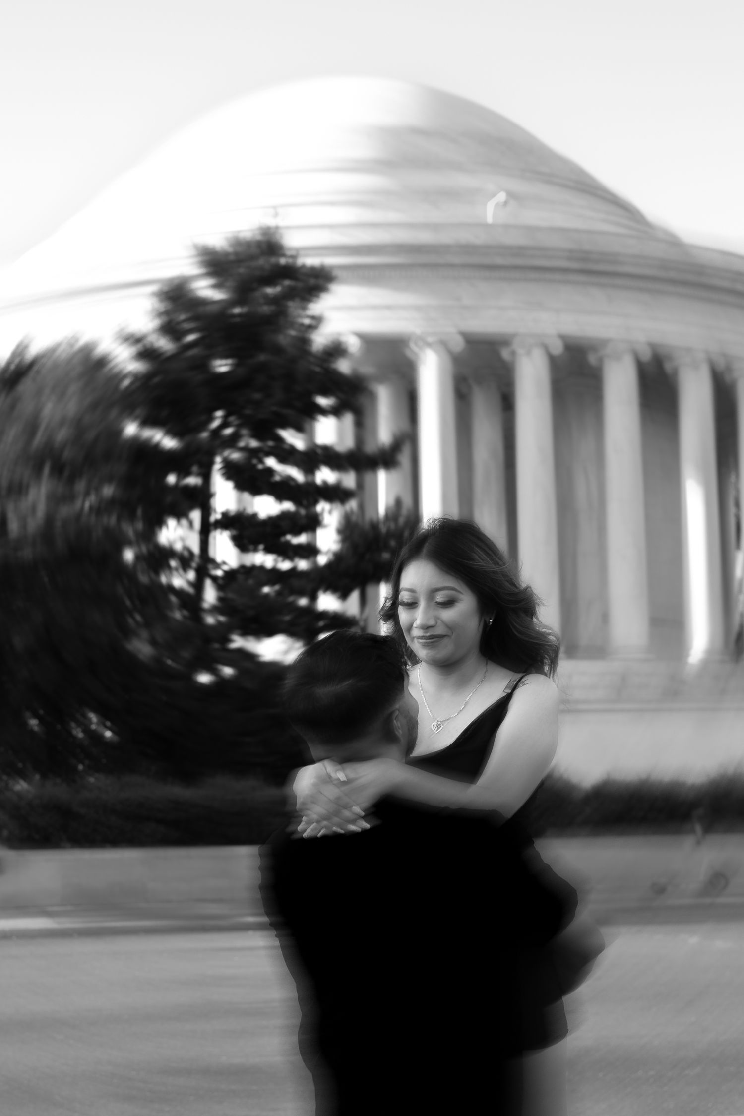 A couple dances in elegant attire near the Jefferson Memorial in black and white.