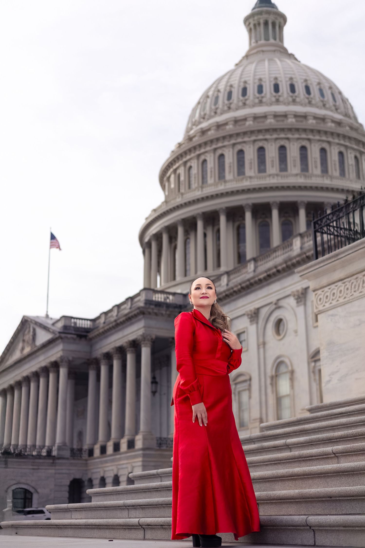 Figure in striking red coat dress poses on steps of US Capitol building.
