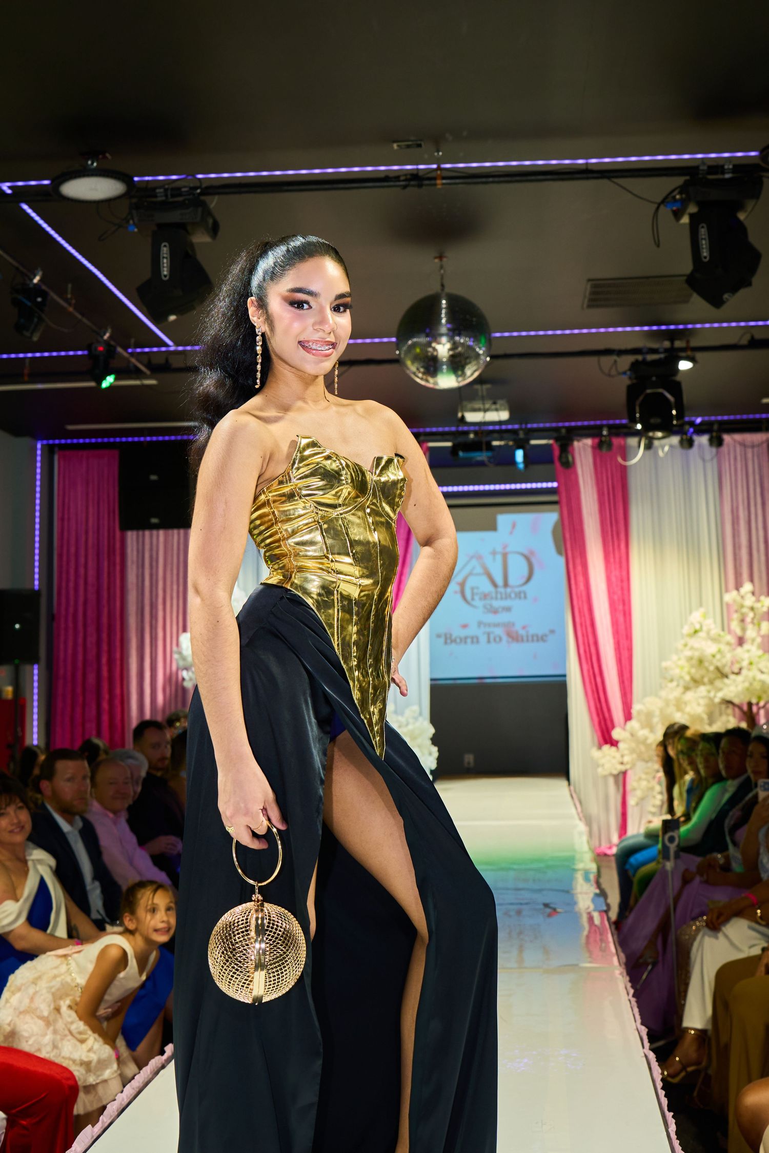Model in gold strapless bodice and black slit skirt gown at AD Fashion runway show.