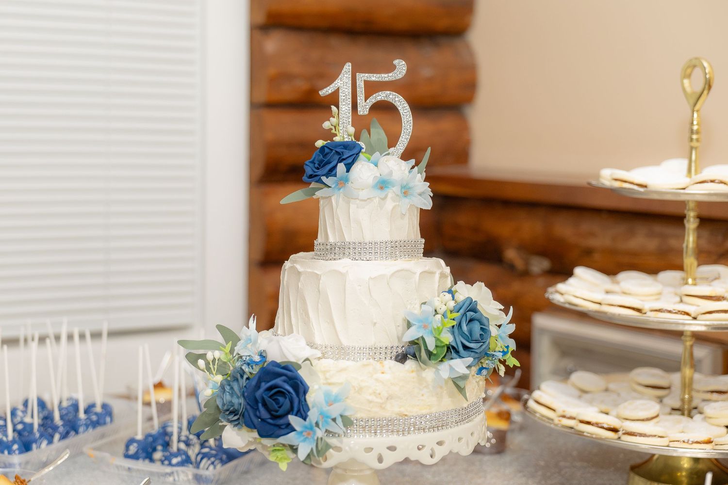 White anniversary cake with blue flowers and silver number 15 topper on rustic wooden background.