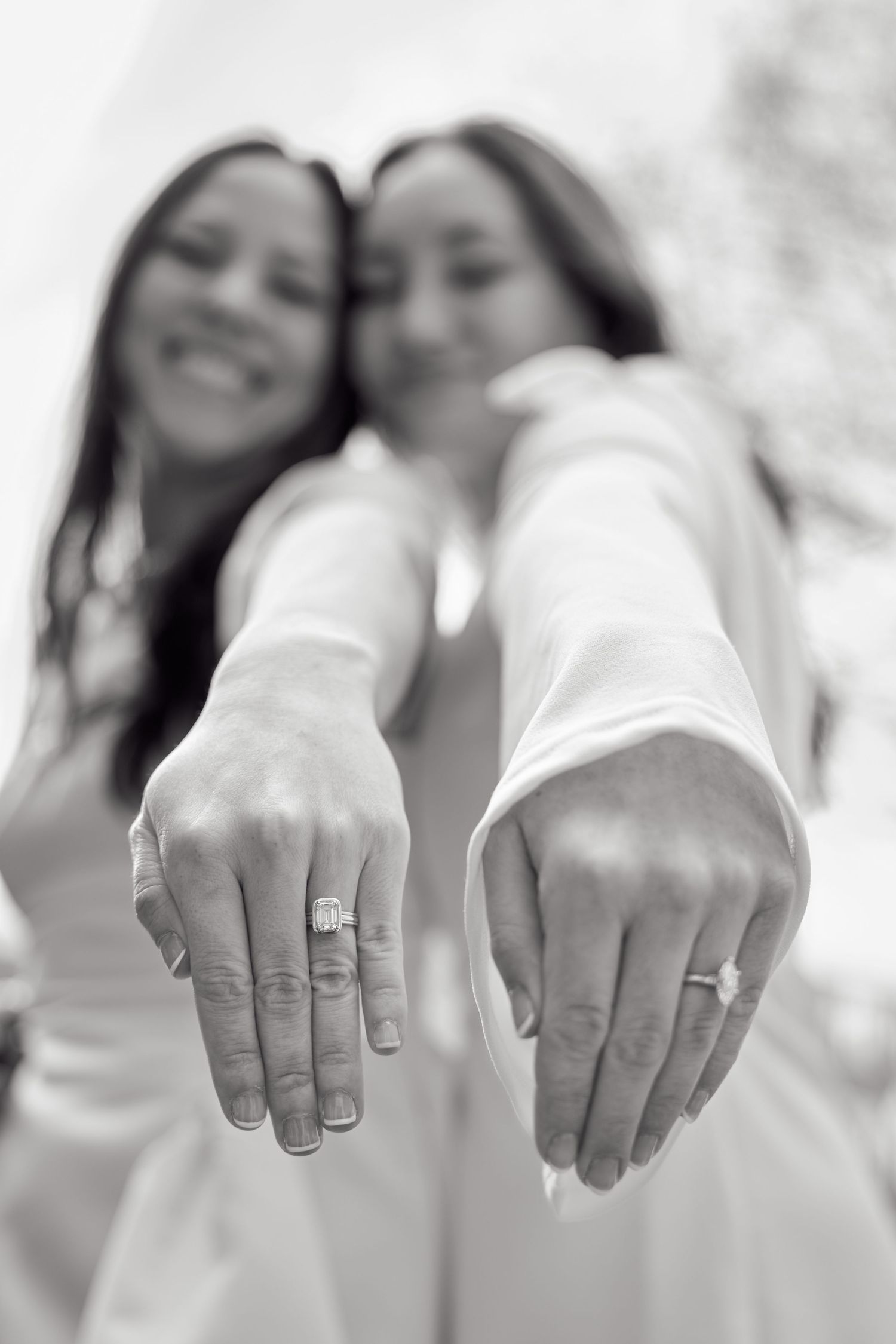 Black and white photo showing hands displaying engagement rings in a row, demonstrating wedding jewelry details.