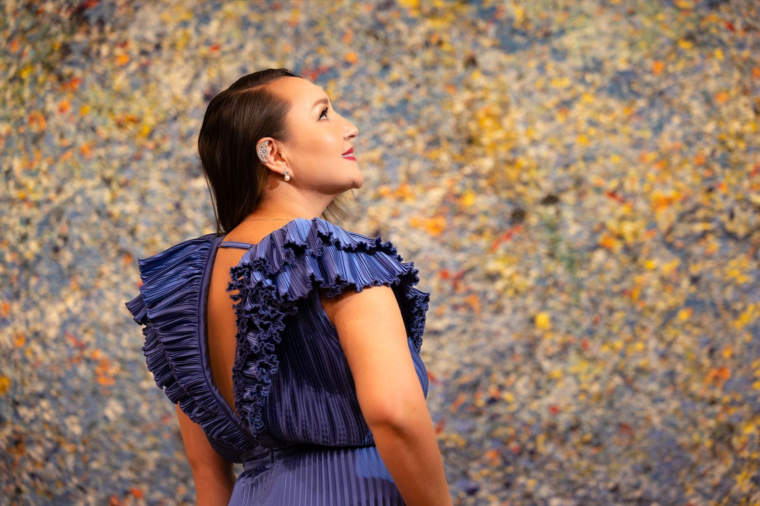 Profile view of pleated navy dress with ruffled detail against artistic backdrop.