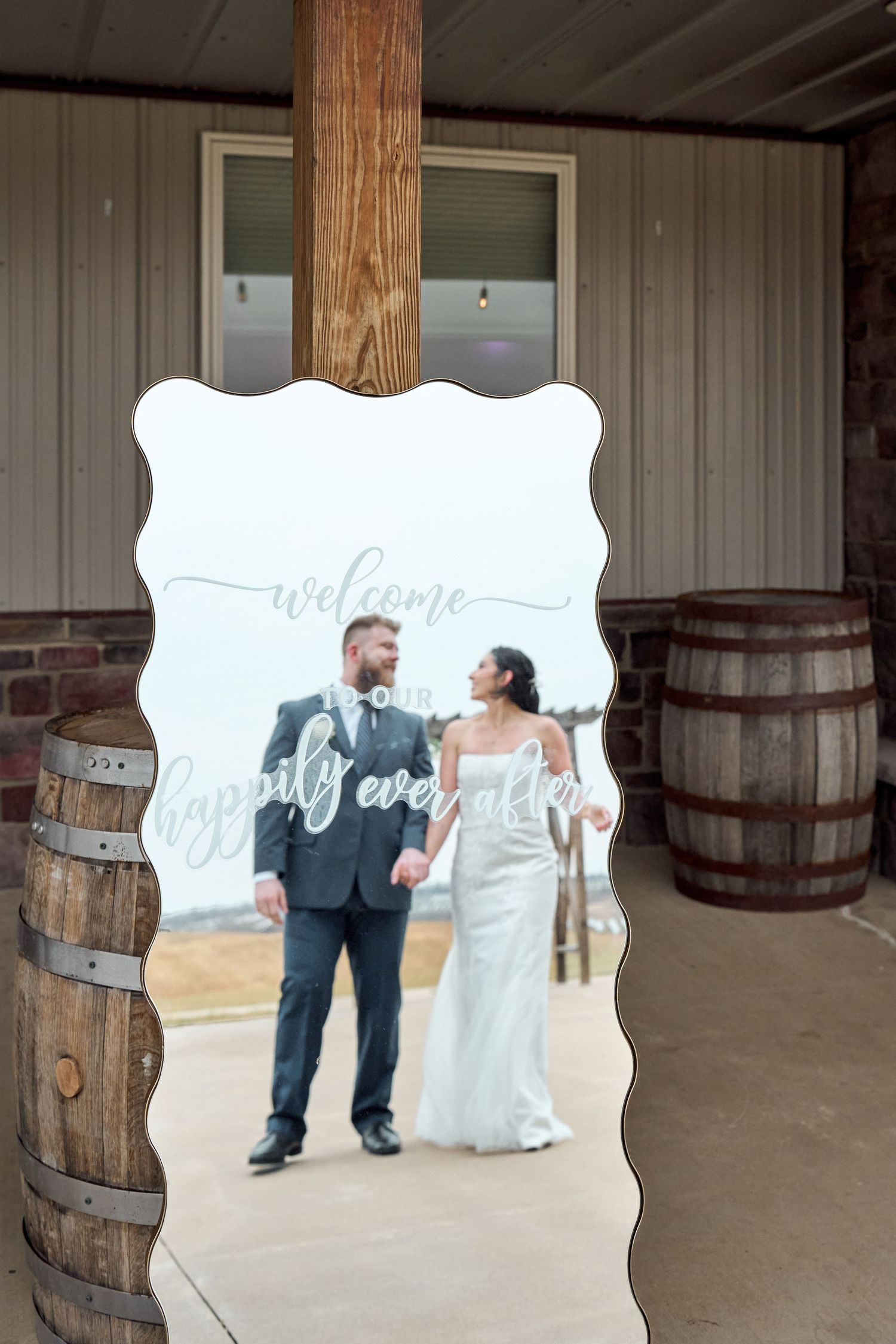 A decorative mirror framed by wooden barrels reflects a couple in formal attire.