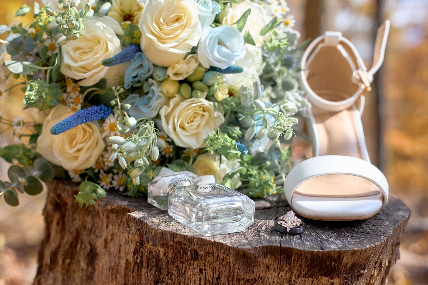 Wedding details featuring white roses and greenery arranged on a rustic wood slice with bridal shoes.