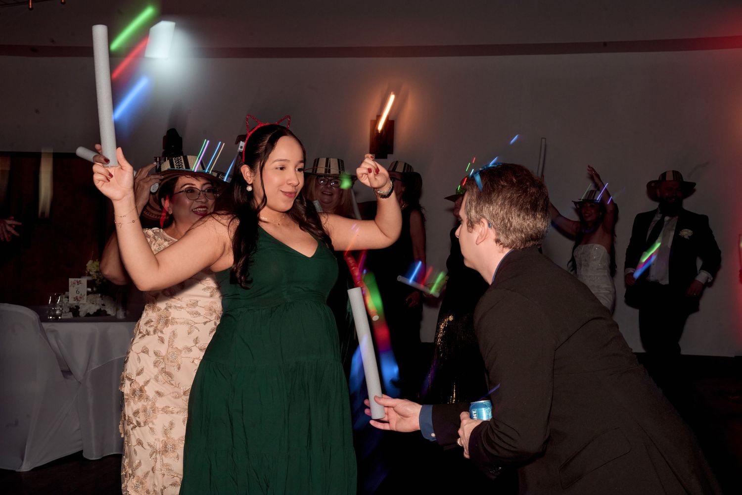 Wedding reception guests dancing with colorful light-up sticks on the dance floor.