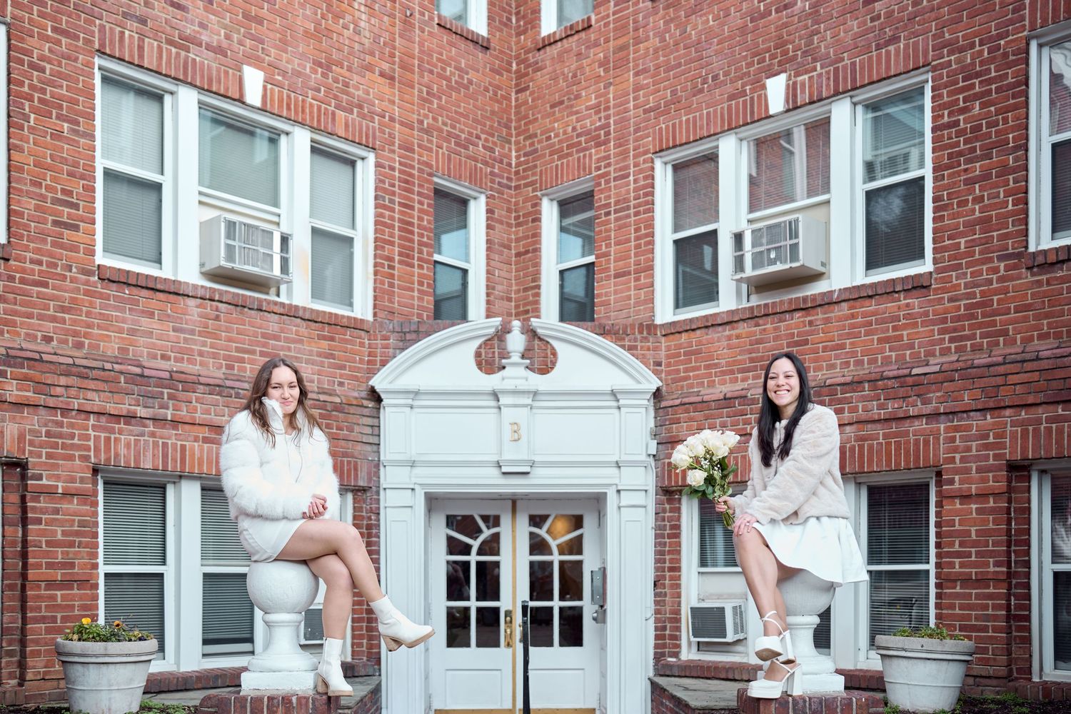 Wedding party poses in front of red brick building with white accents and windows.