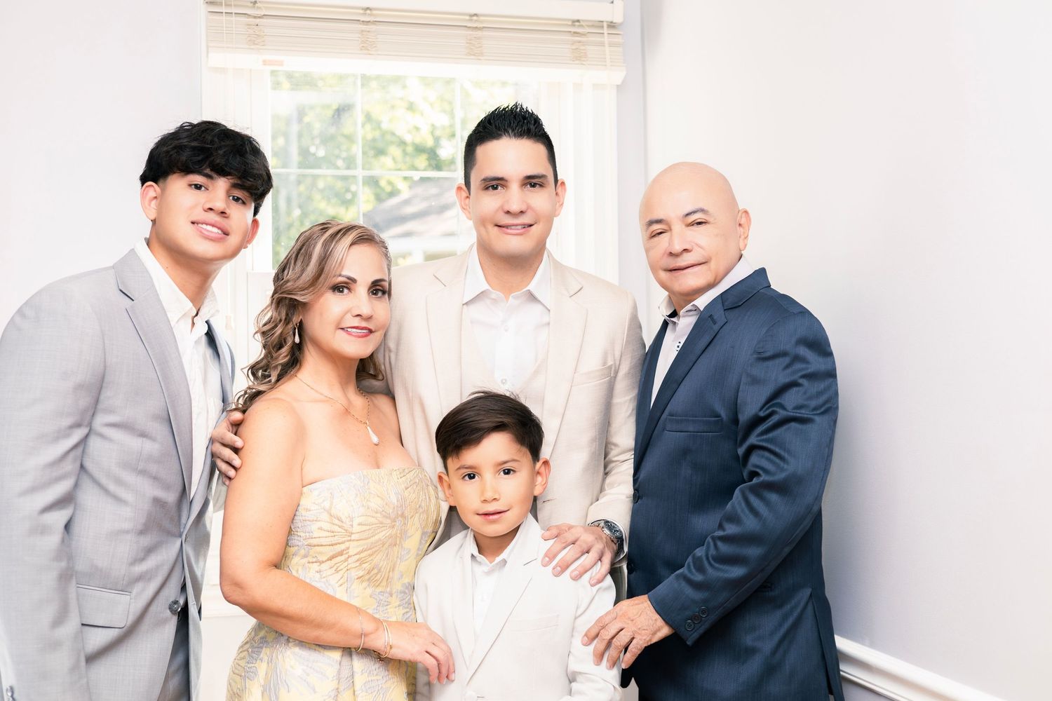 Wedding party members posing together in light-colored formal wear against a white wall.
