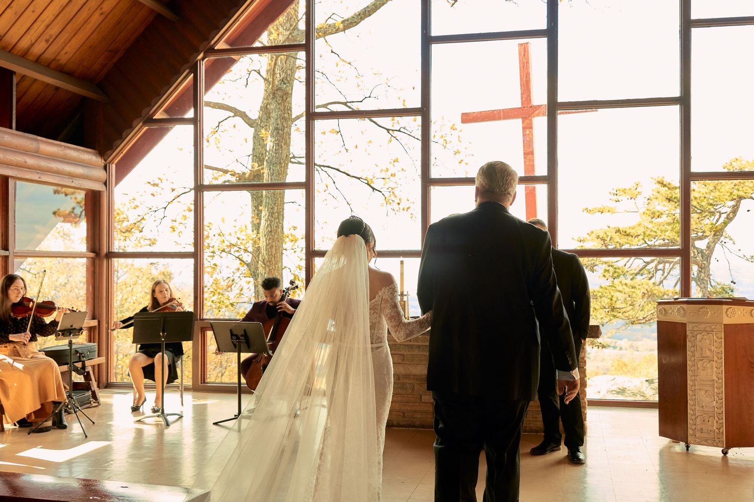 Elegant indoor wedding ceremony with large windows overlooking autumn trees and natural light filling the space.