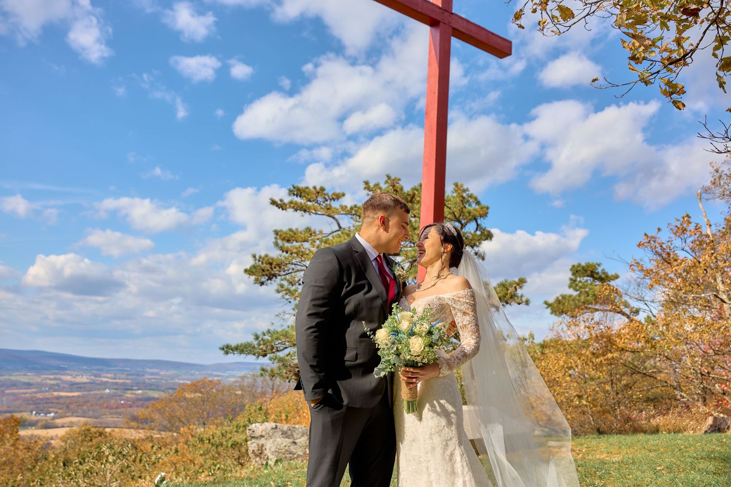 Couple shares romantic moments in scenic fall mountain setting with vibrant autumn foliage and blue skies.