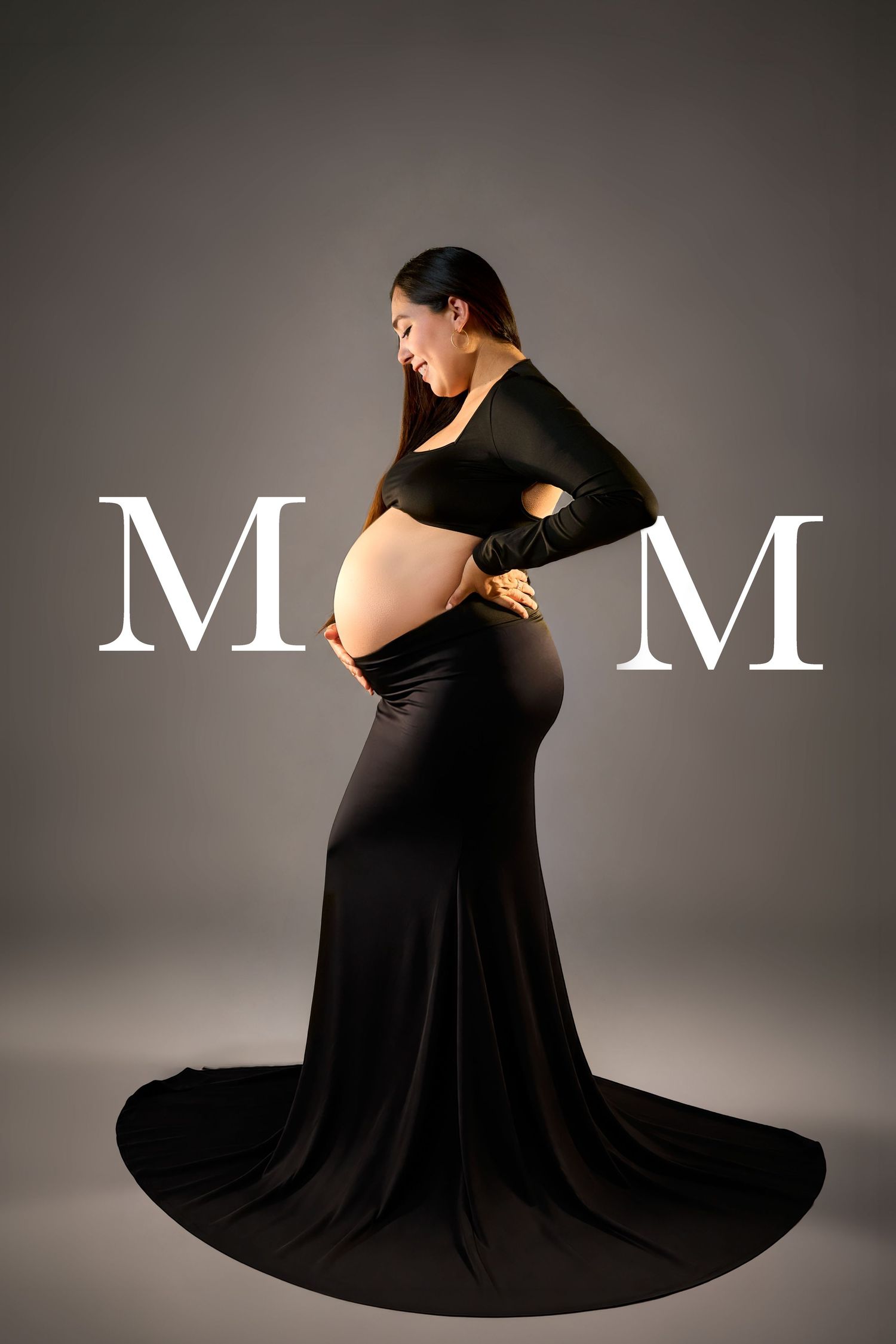 Pregnant woman in elegant black maternity gown posing with hands on belly in studio with MOM text.