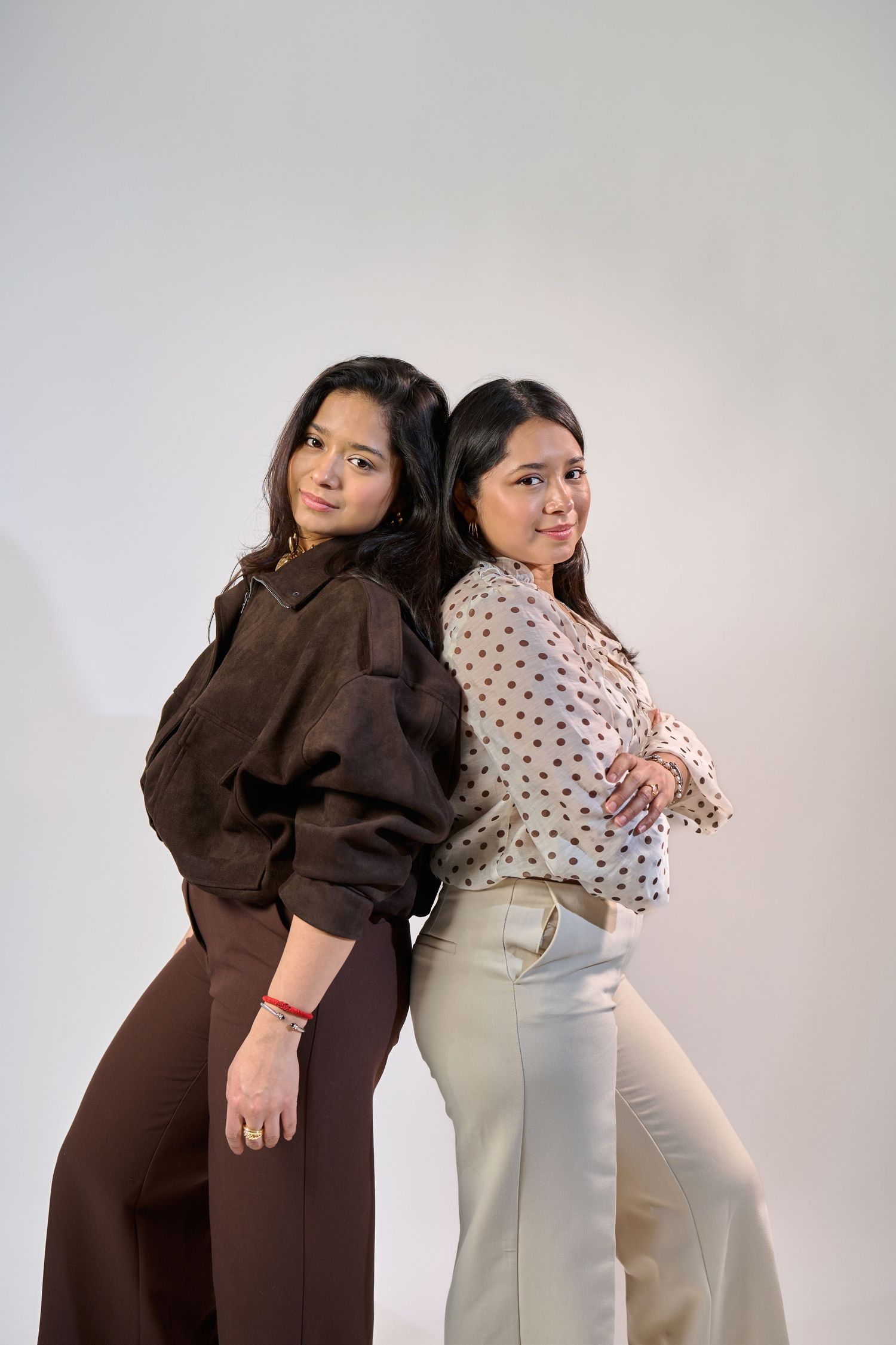 Two women in contrasting brown and polka dot outfits pose playfully against a white backdrop in a fashion photoshoot.