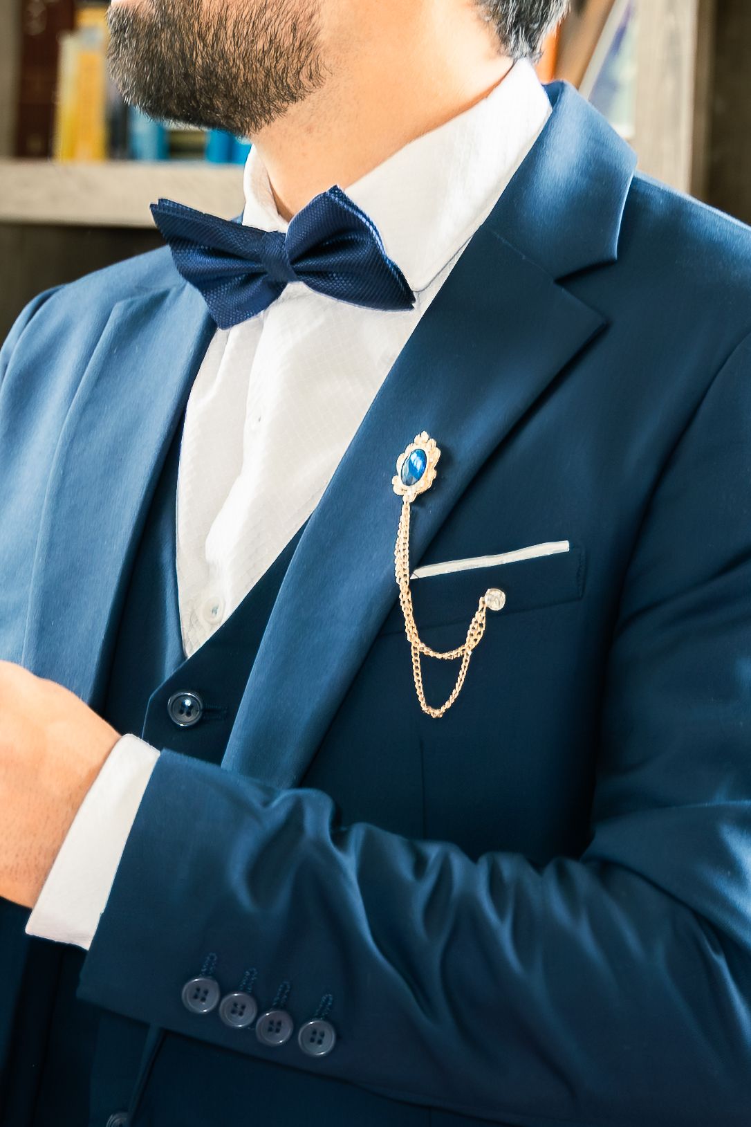 Close-up of navy blue suit jacket with matching bow tie and decorative chain brooch on white dress shirt.