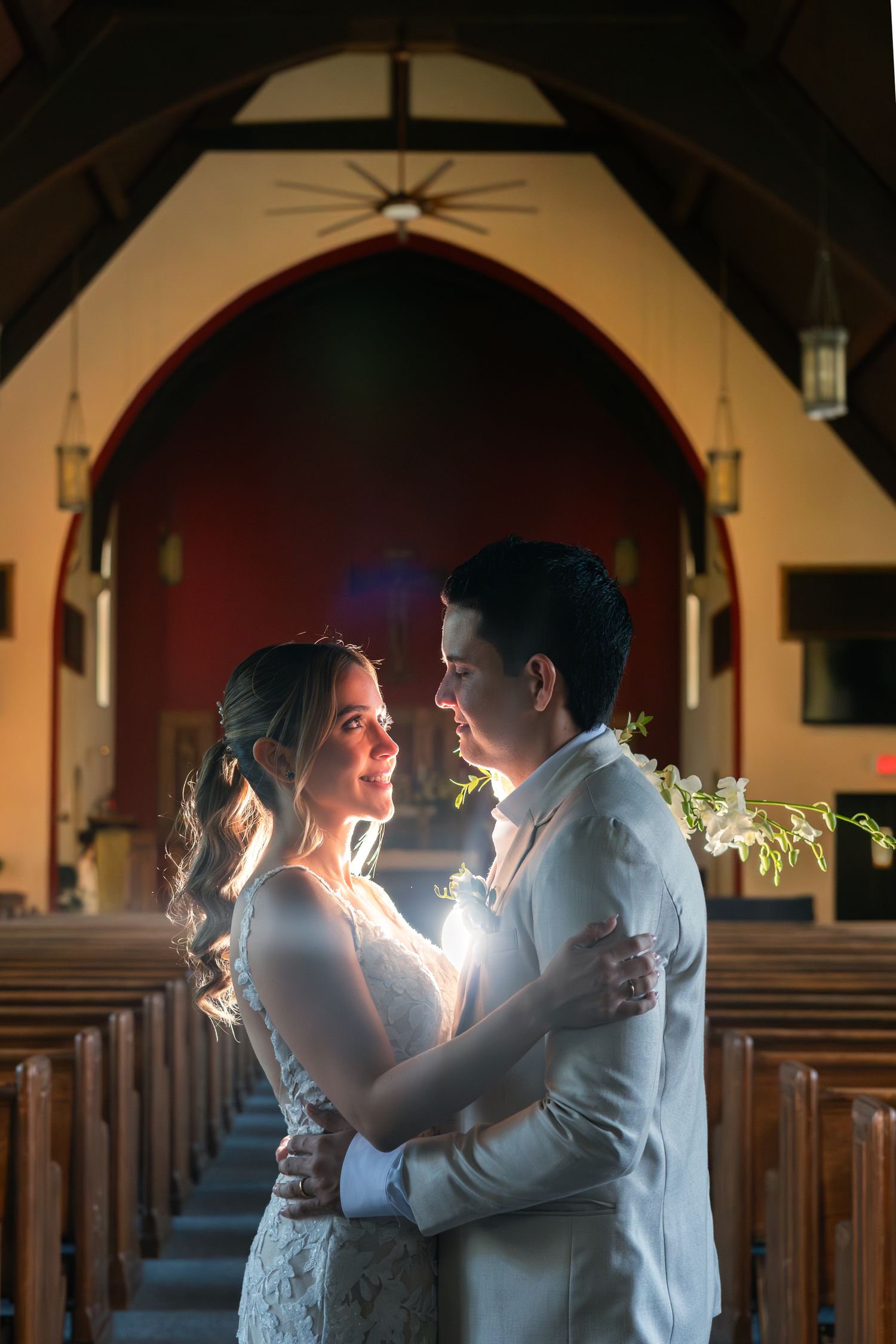 A couple shares an intimate moment in dramatic lighting inside a church sanctuary during their wedding photoshoot.