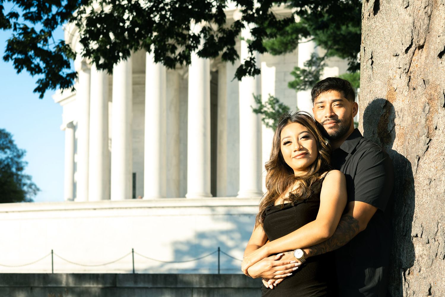 A couple embraces near white stone columns on a sunny day outdoors.