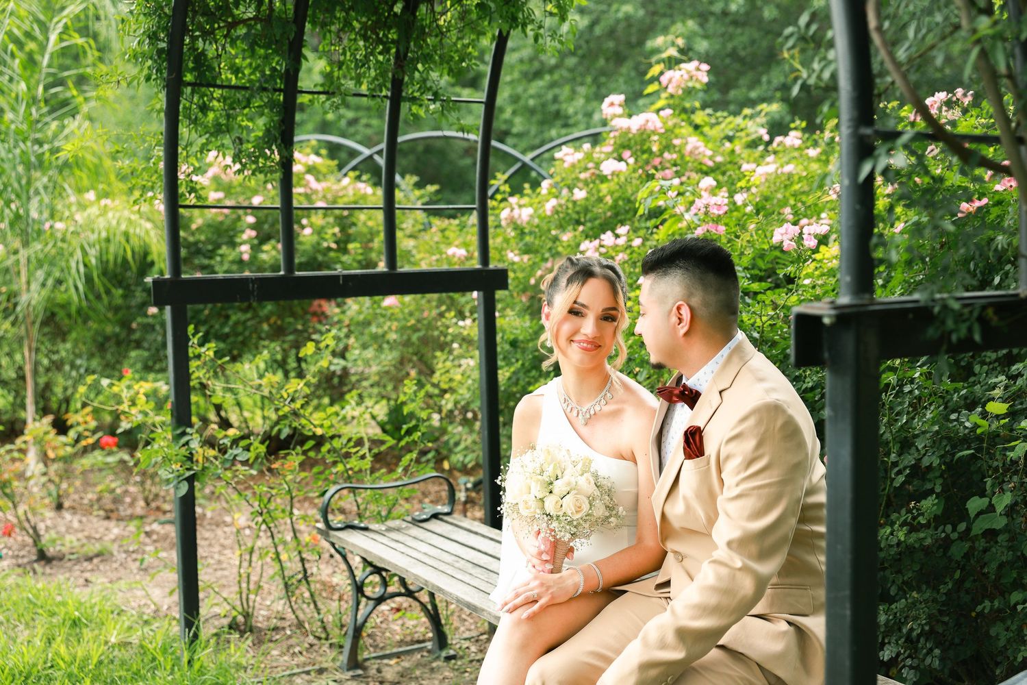 A couple shares romantic moments in a lush garden setting with blooming flowers and greenery.