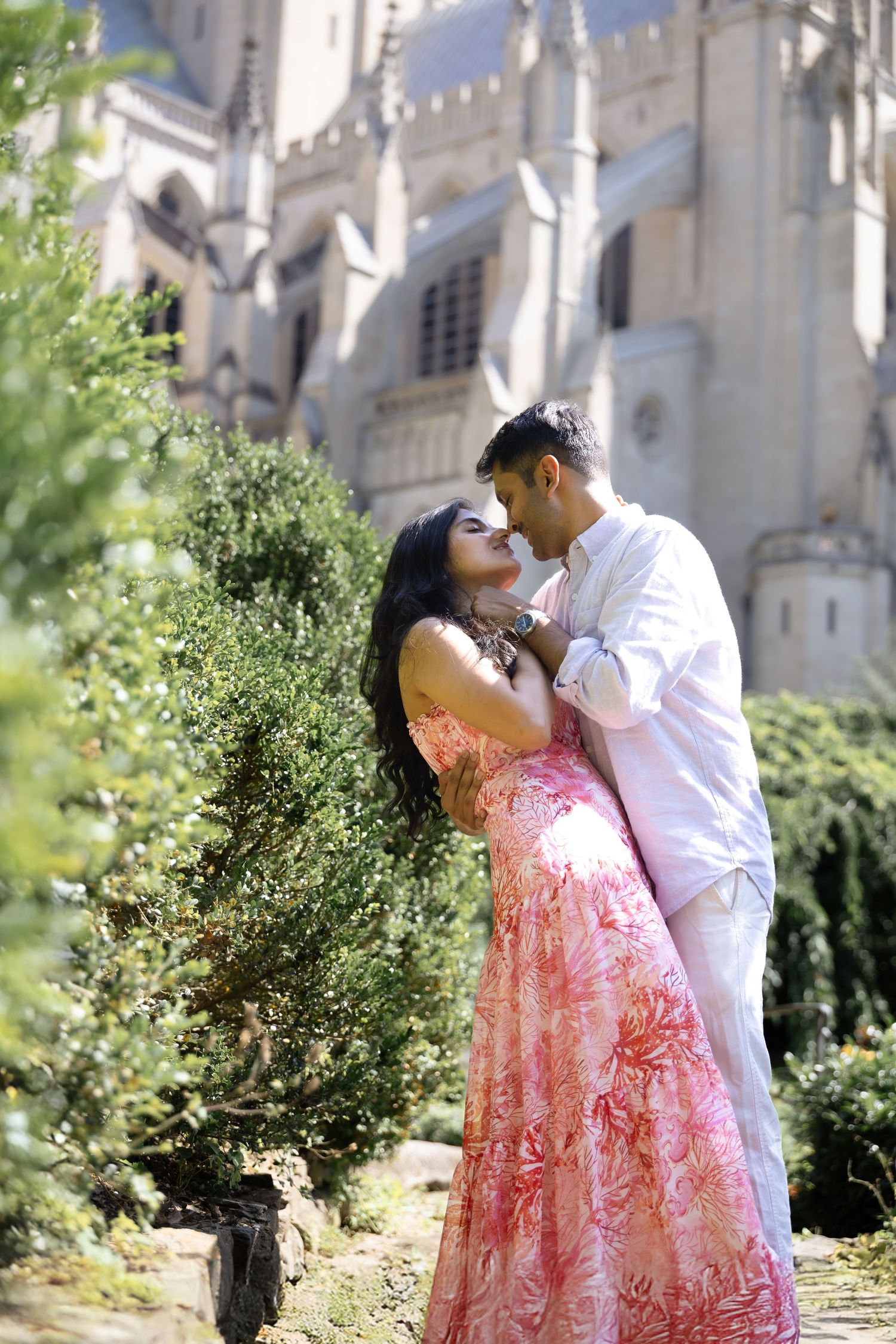 Romantic couple sharing intimate moments in a garden setting with elegant architecture in the background.