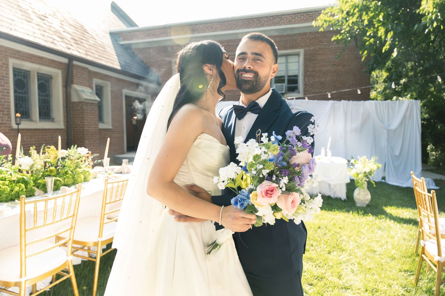Wedding couple shares a romantic first dance outdoors in a sunlit garden setting surrounded by floral arrangements.