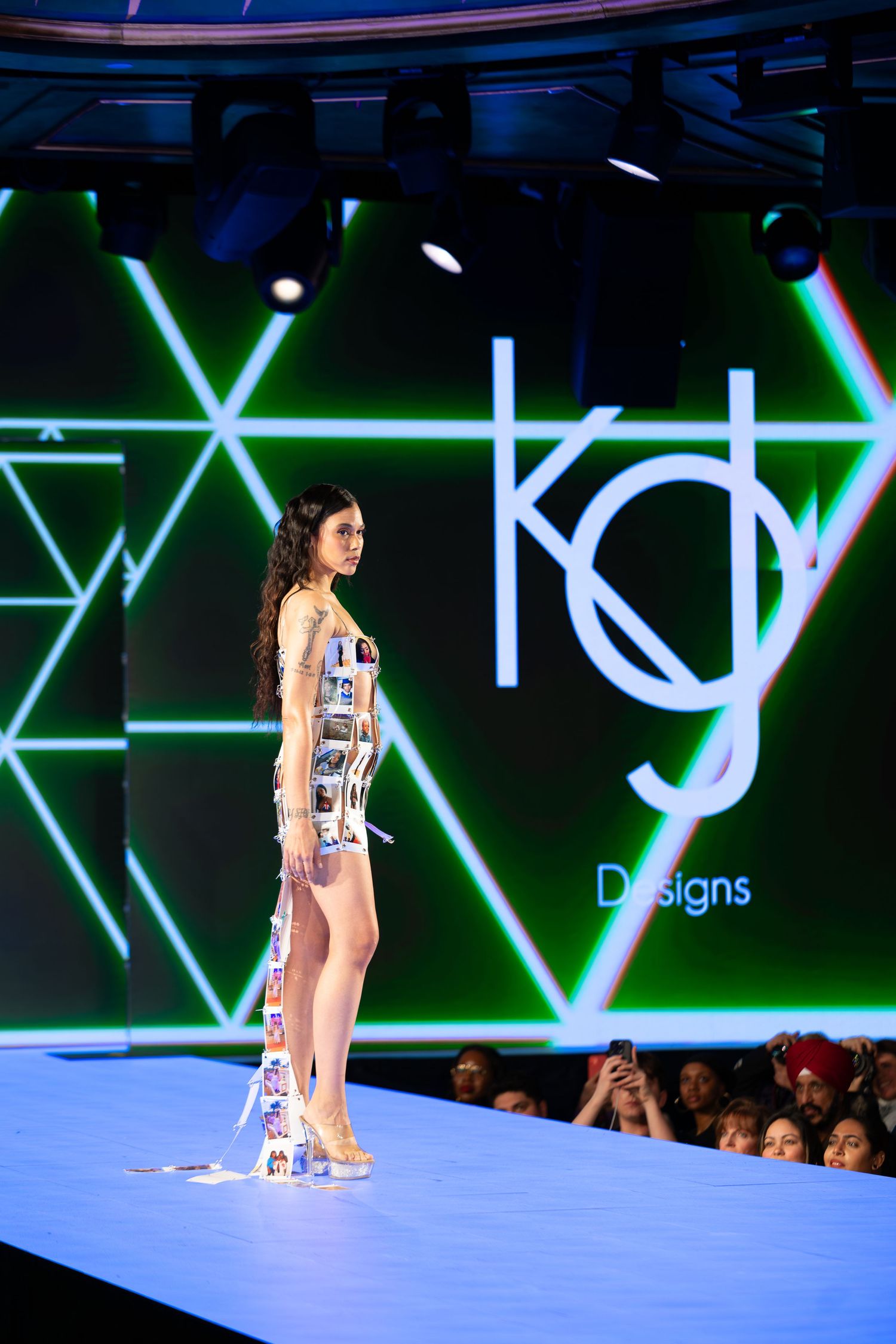 Model in geometric print mini dress walks runway with neon lighting display backdrop.
