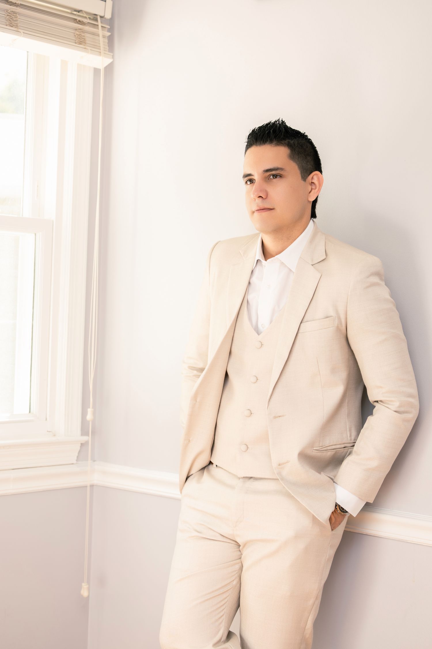 A person in a cream-colored suit poses against a white wall in multiple artistic shots.