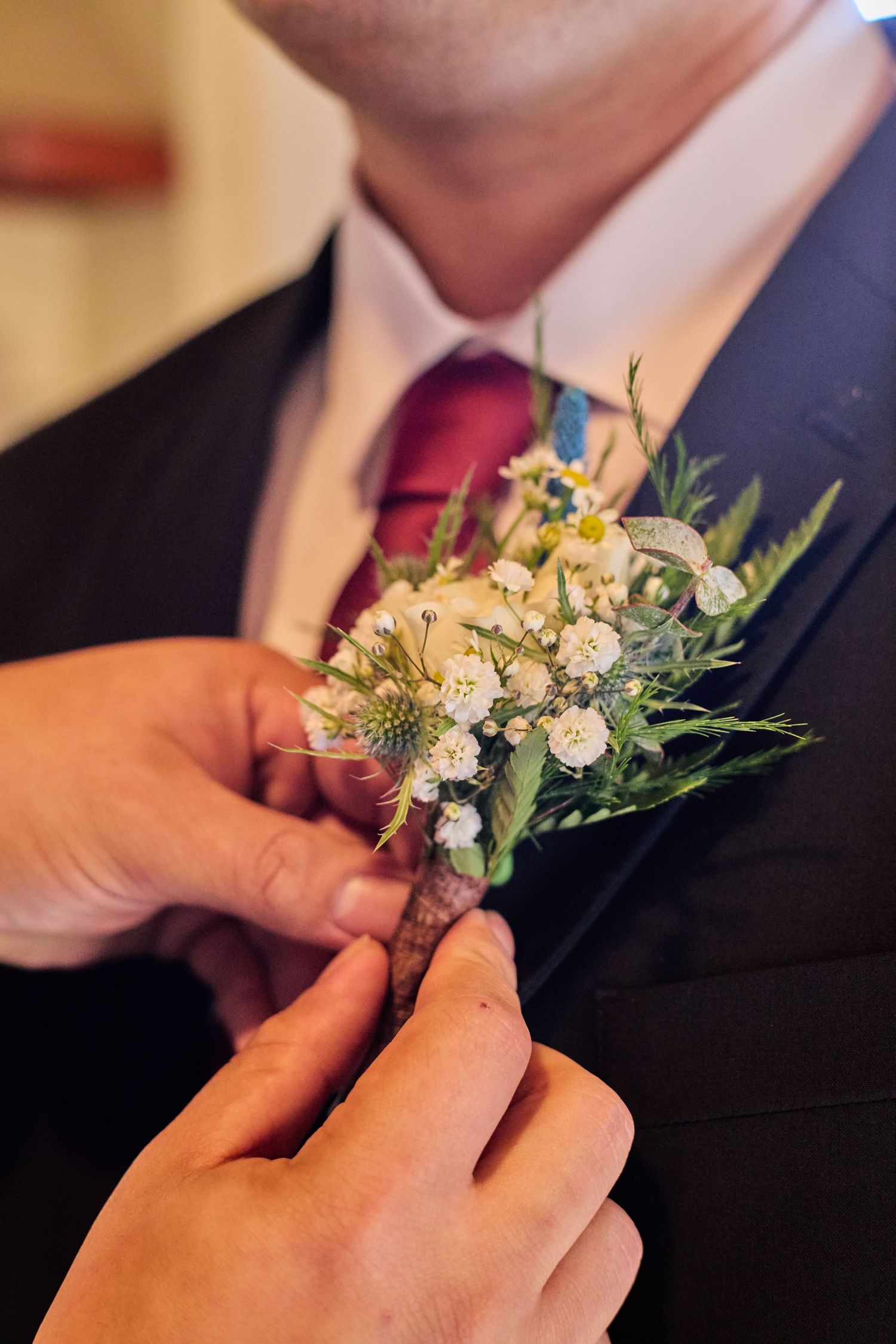 Close-up sequence showing hands pinning a delicate white floral boutonniere onto a black suit jacket.