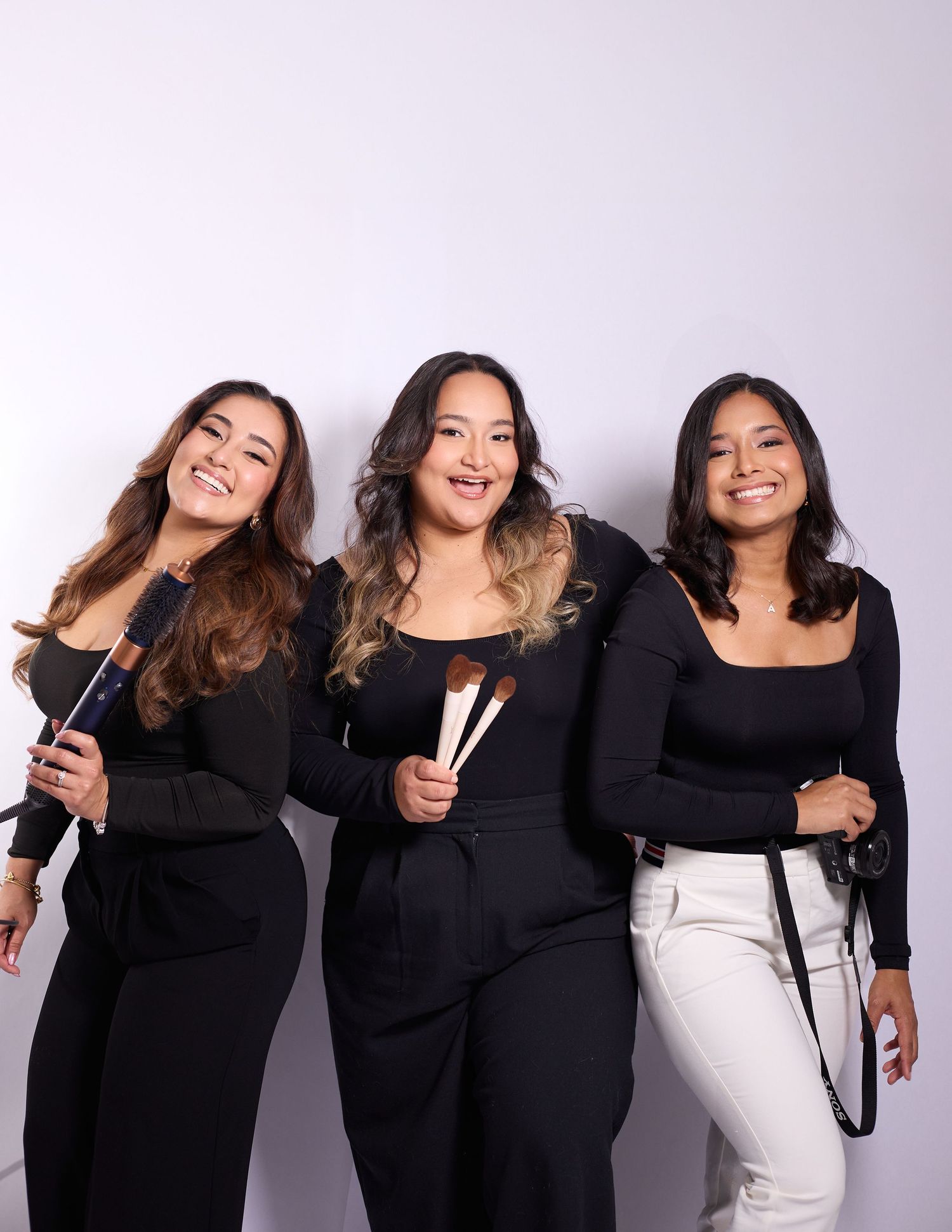 A group of women in black outfits strike fun poses together against a white backdrop in a series of connected photos.