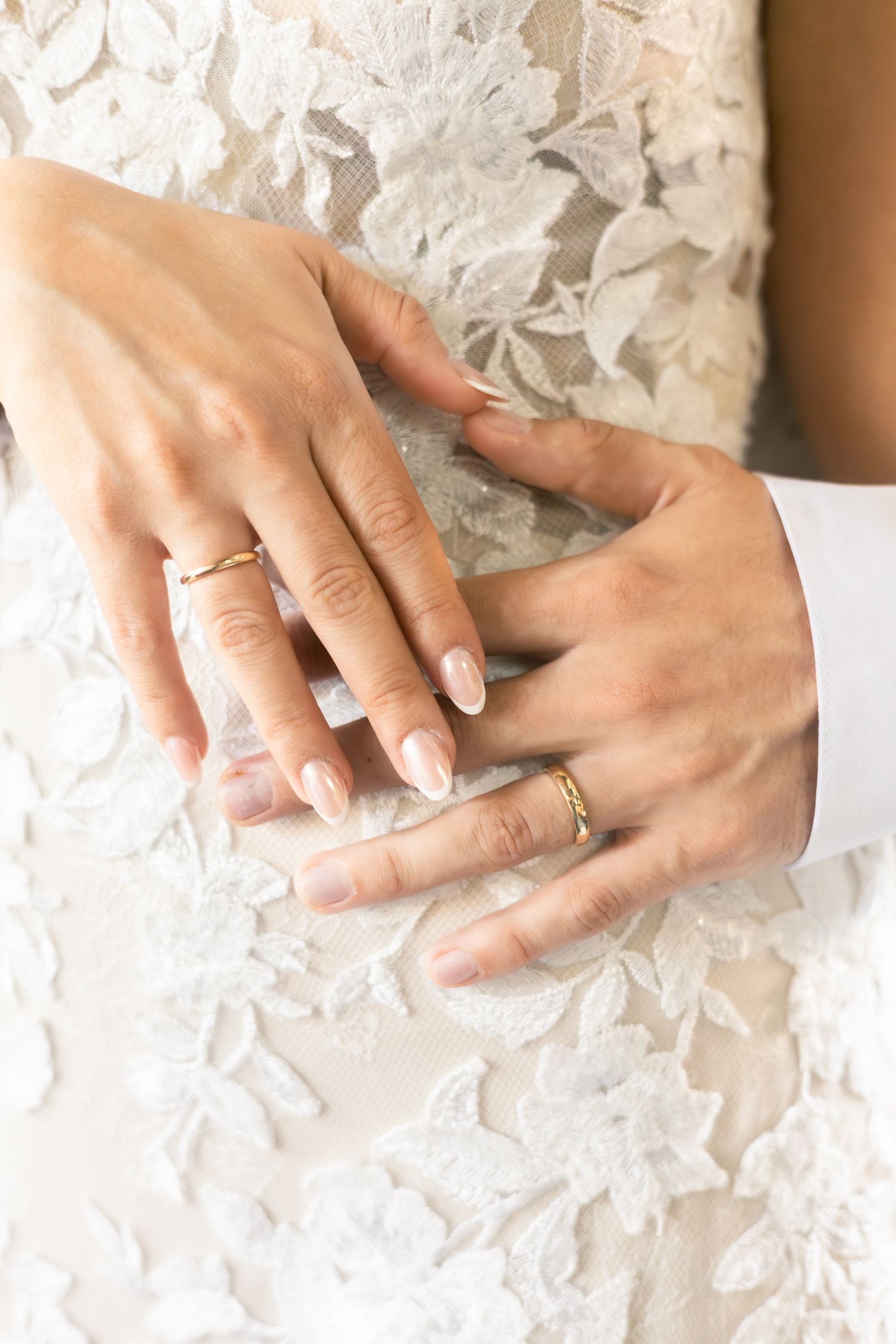 Close-up of hands with a wedding ring against delicate white lace fabric creating an elegant bridal detail.