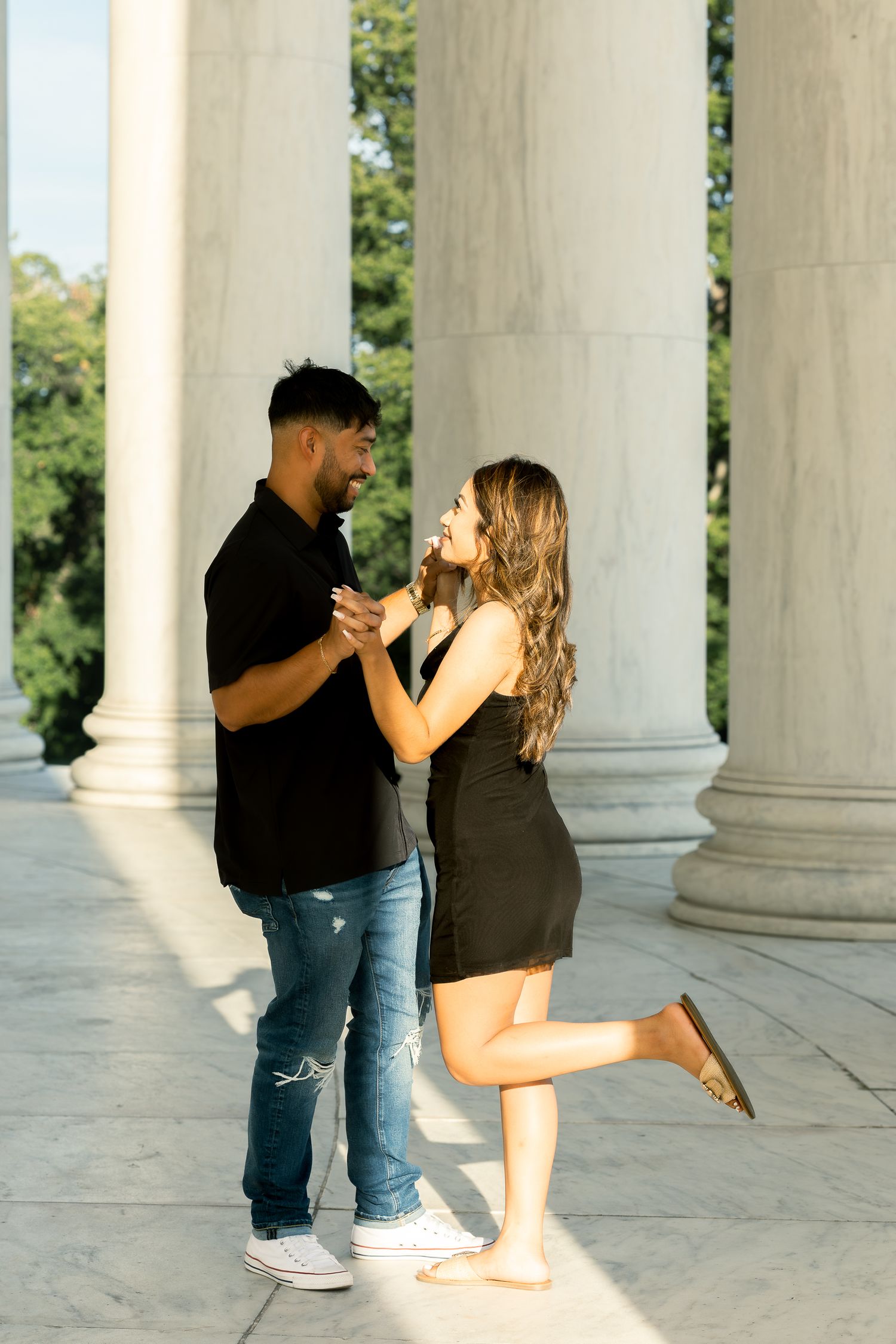 Couple shares playful moments together among white classical columns in an outdoor setting.