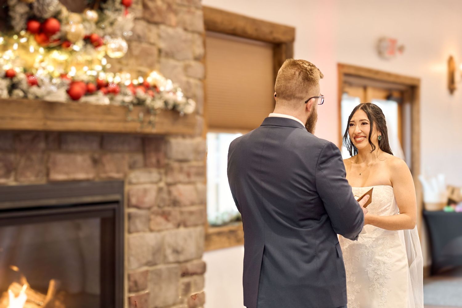 A couple shares their first look moment in front of a stone fireplace decorated with floral arrangements.
