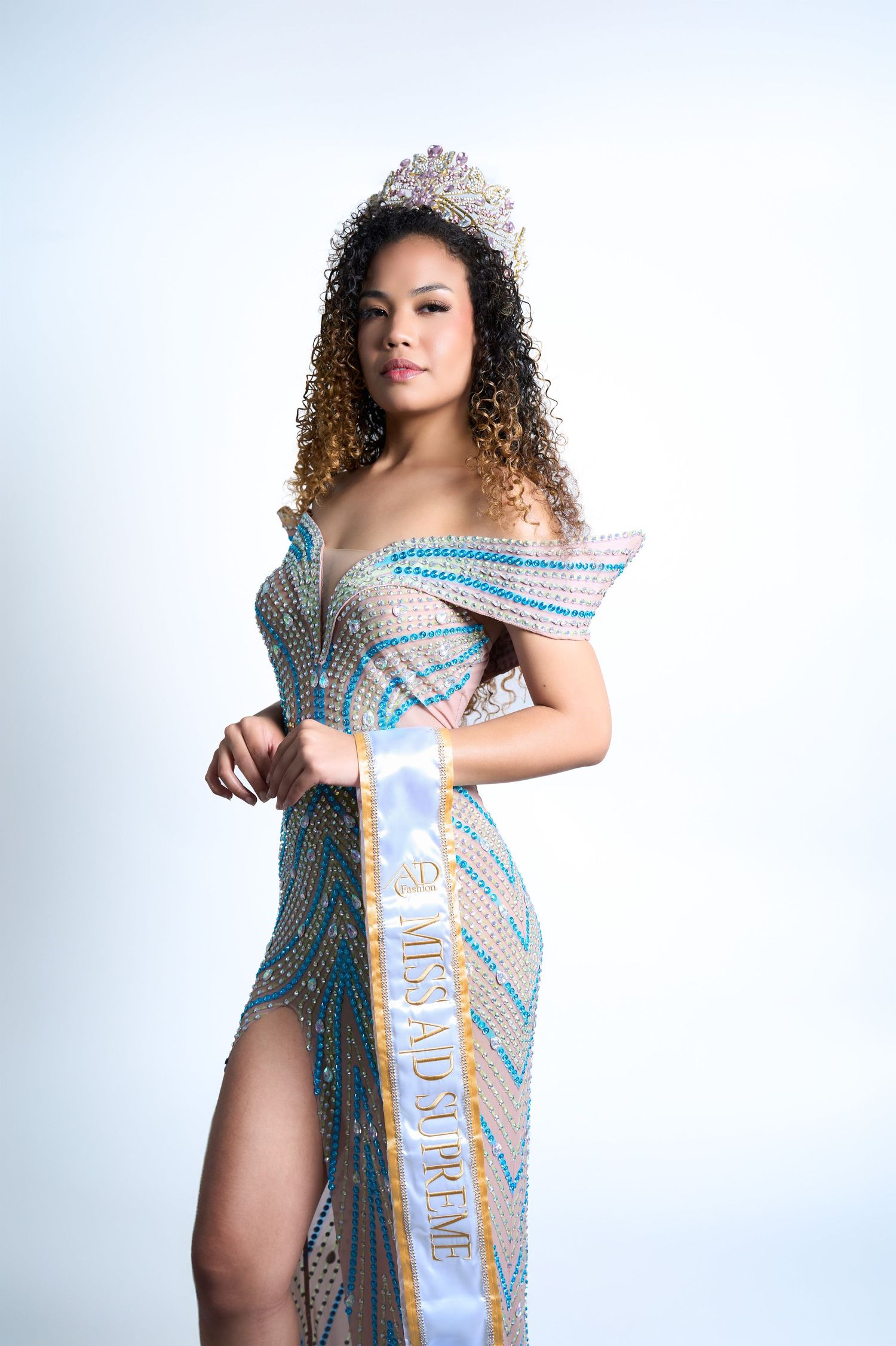 Young woman in a sparkling gown, crown, and Miss AD Premier sash poses confidently against a white background.